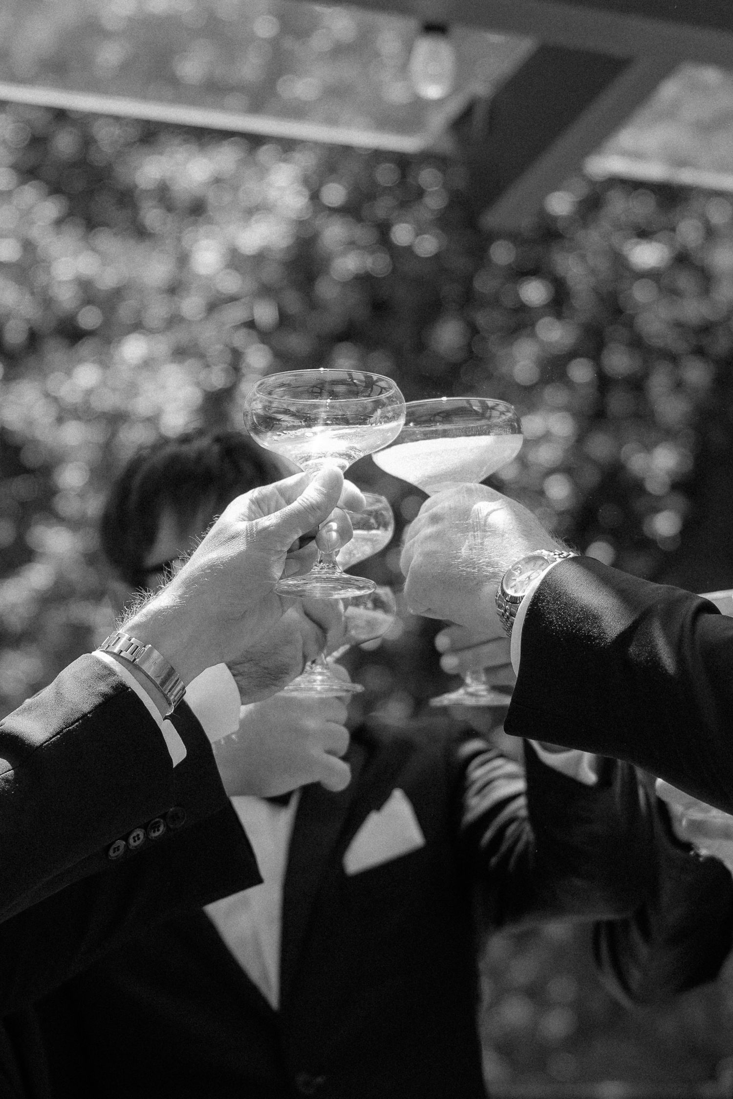 Hands raise champagne glasses in a celebratory toast at an elegant black tie event, captured in black and white.