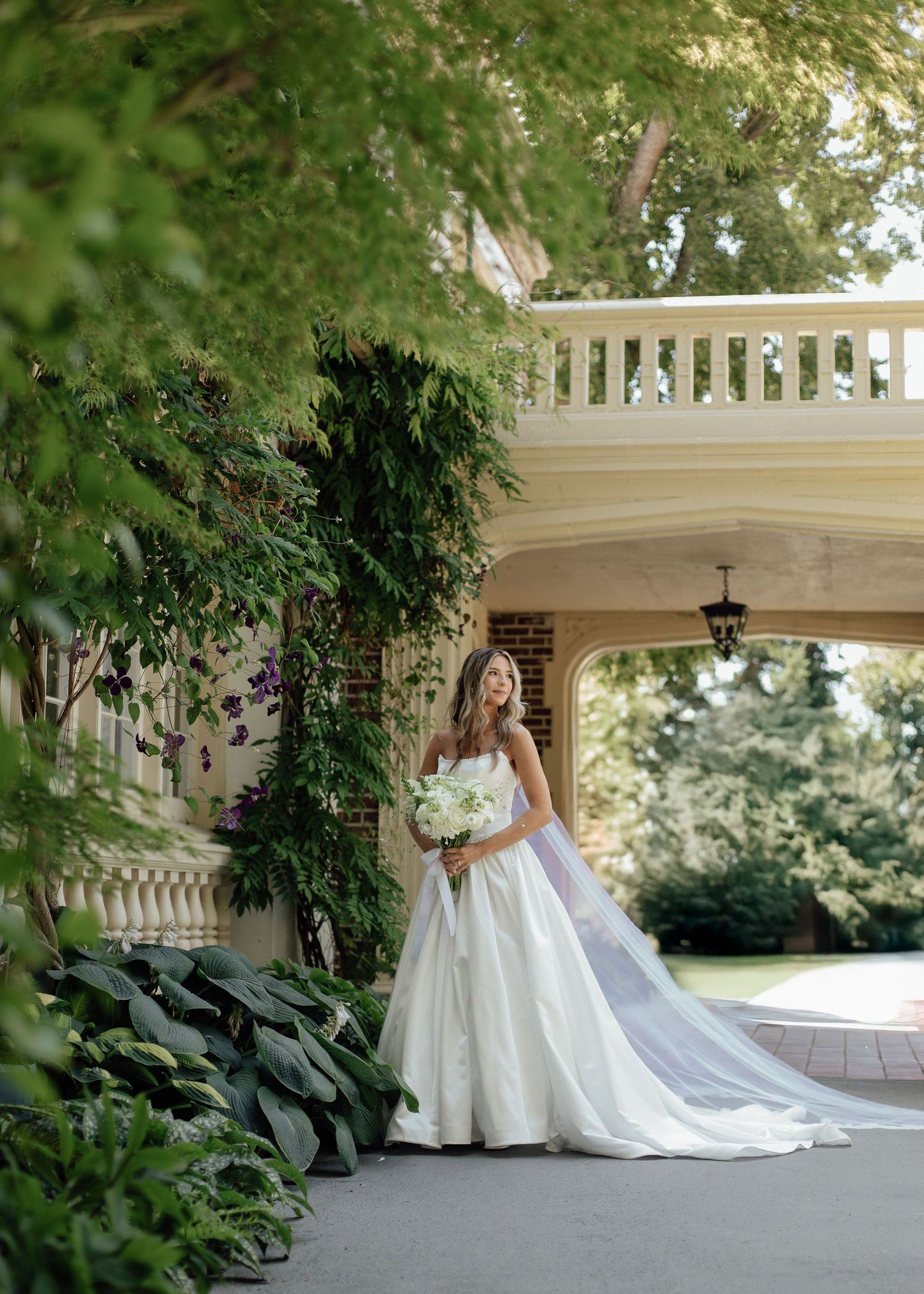 Expansive white wedding gown with a long train photographed in front of a classic covered porch.