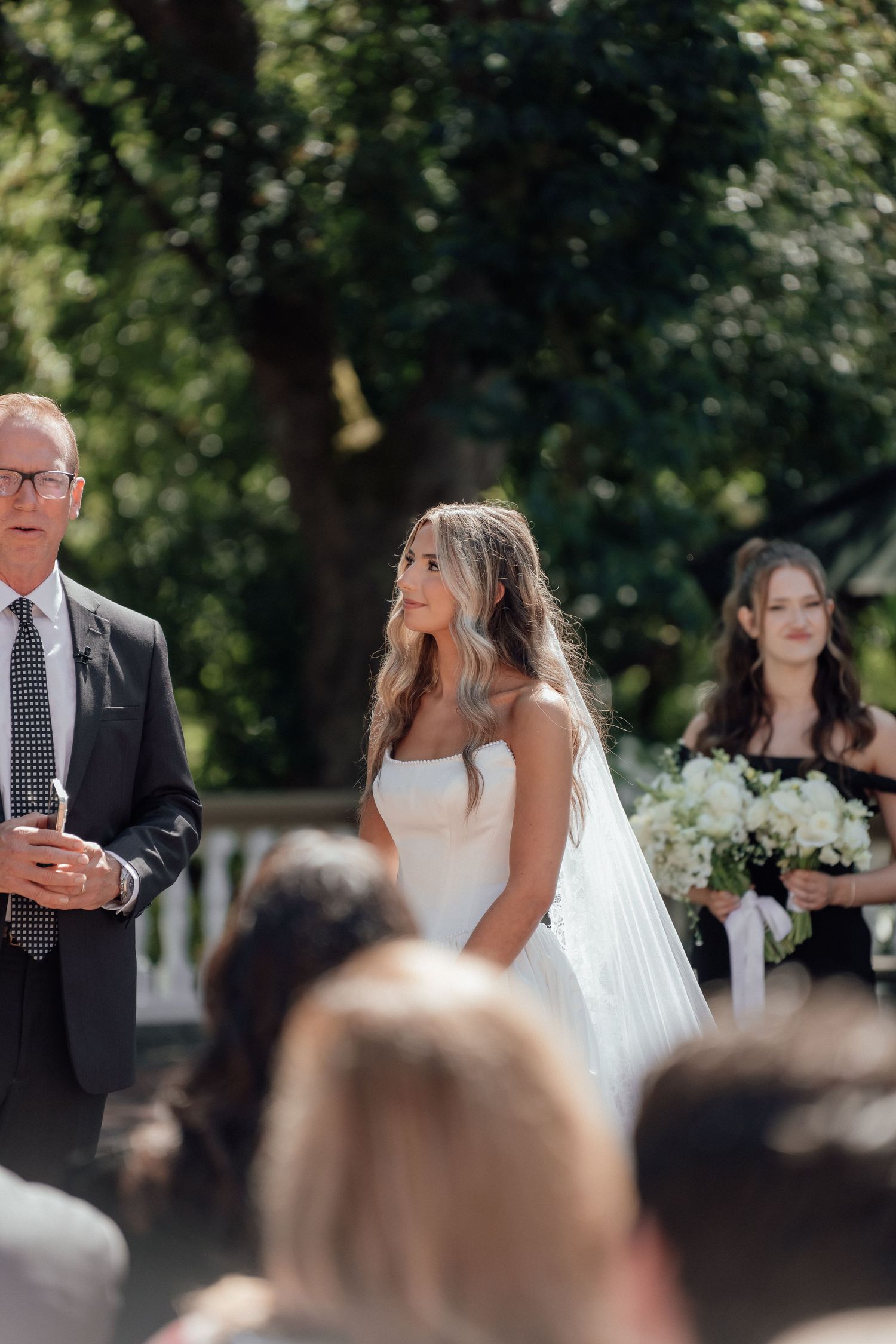 A wedding ceremony in progress on a sunny day with guests seated outdoors.