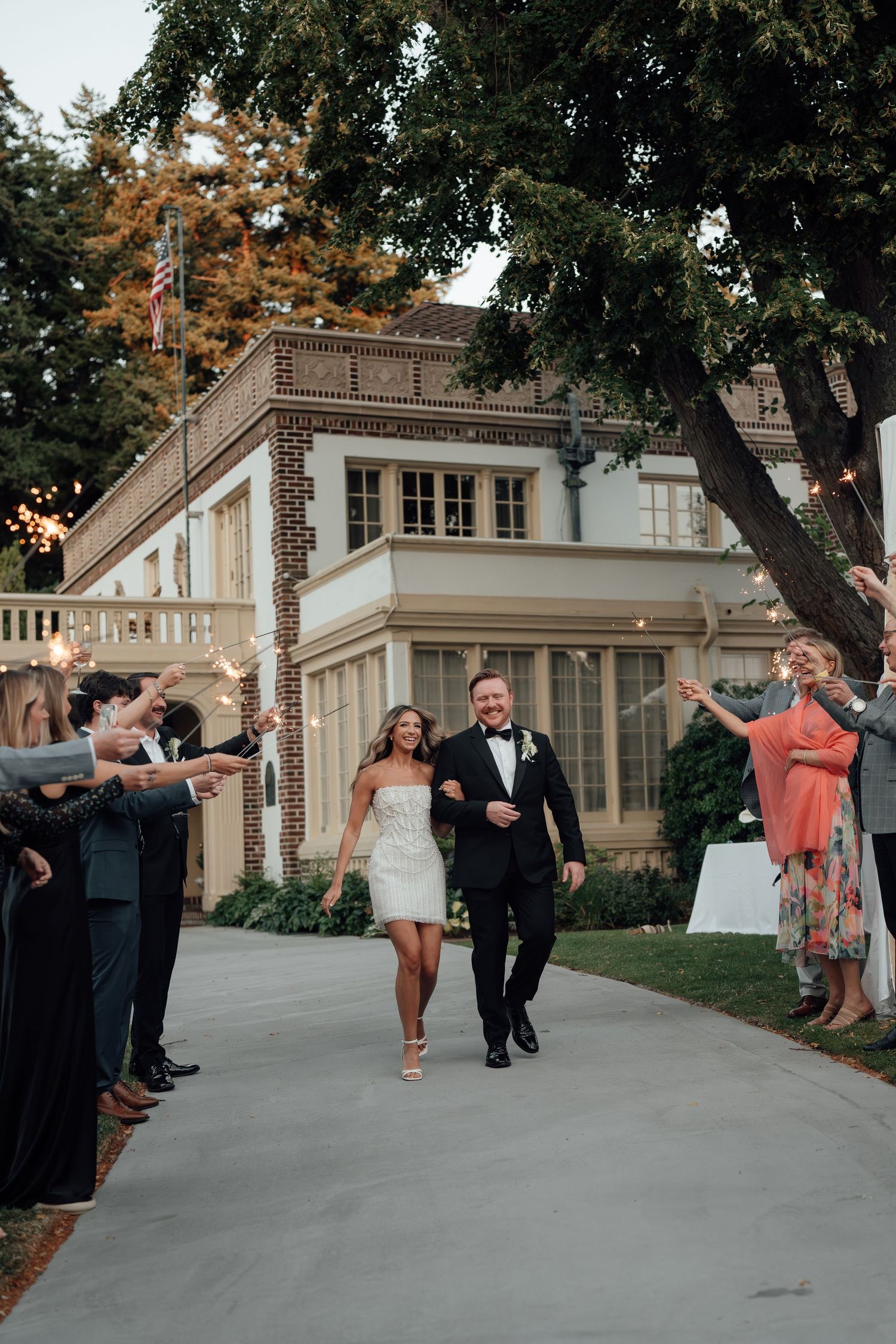 A celebratory wedding exit with guests cheering outside a grand white mansion.