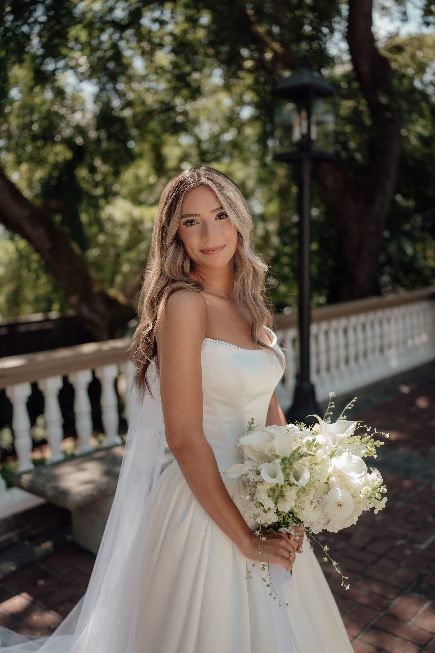 An elegant bridal portrait on a brick terrace featuring a white wedding gown and classic white bouquet.