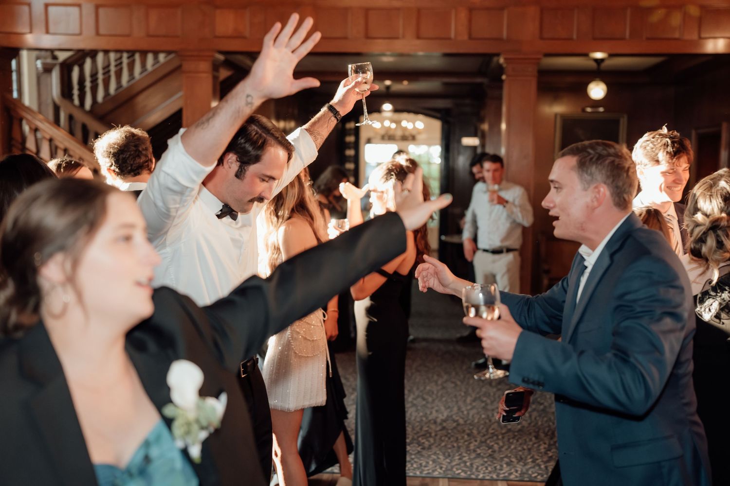 Wedding reception guests raise their hands in celebration during a festive indoor party.