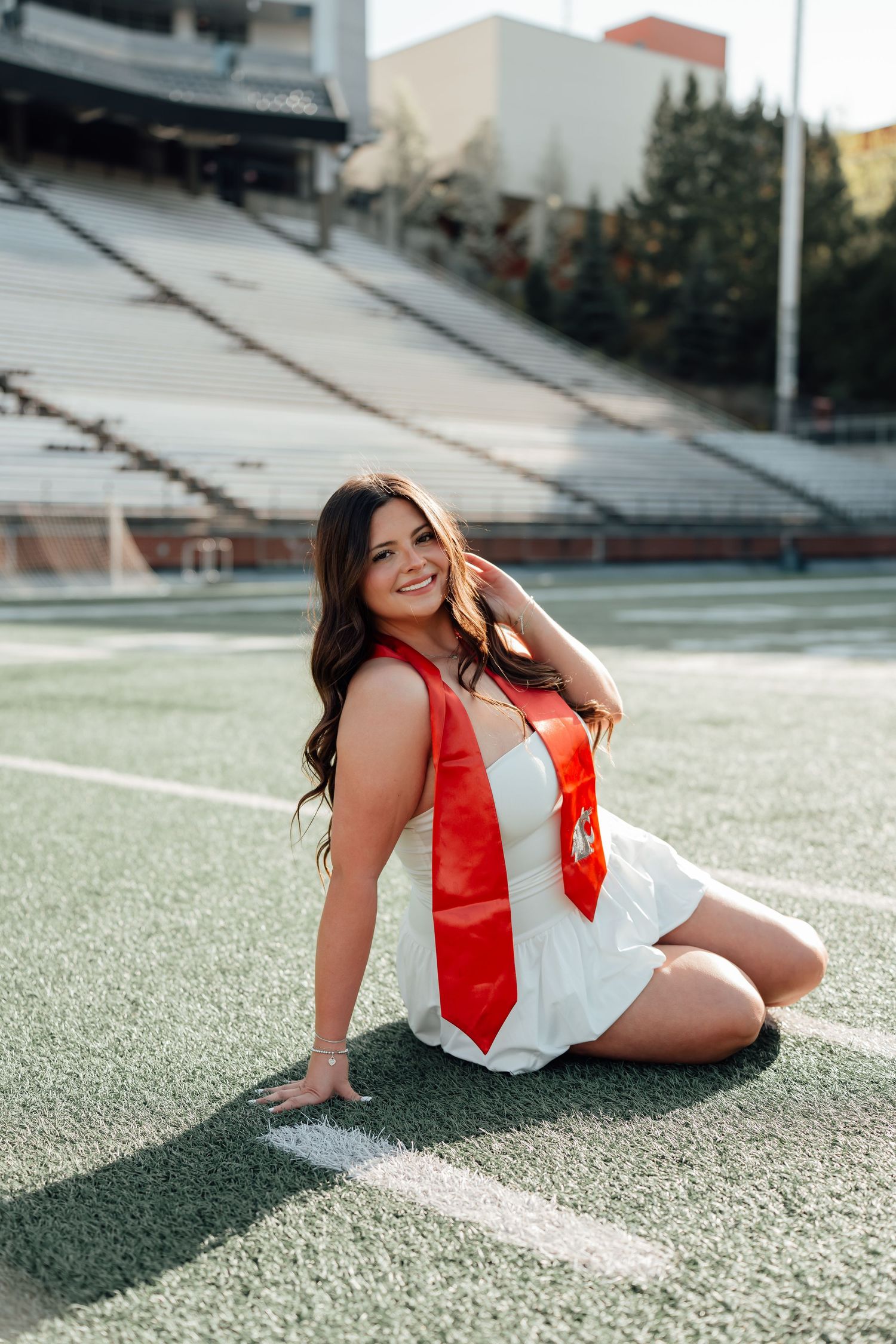 Graduate in red and white attire poses at athletic field during outdoor graduation photo session.