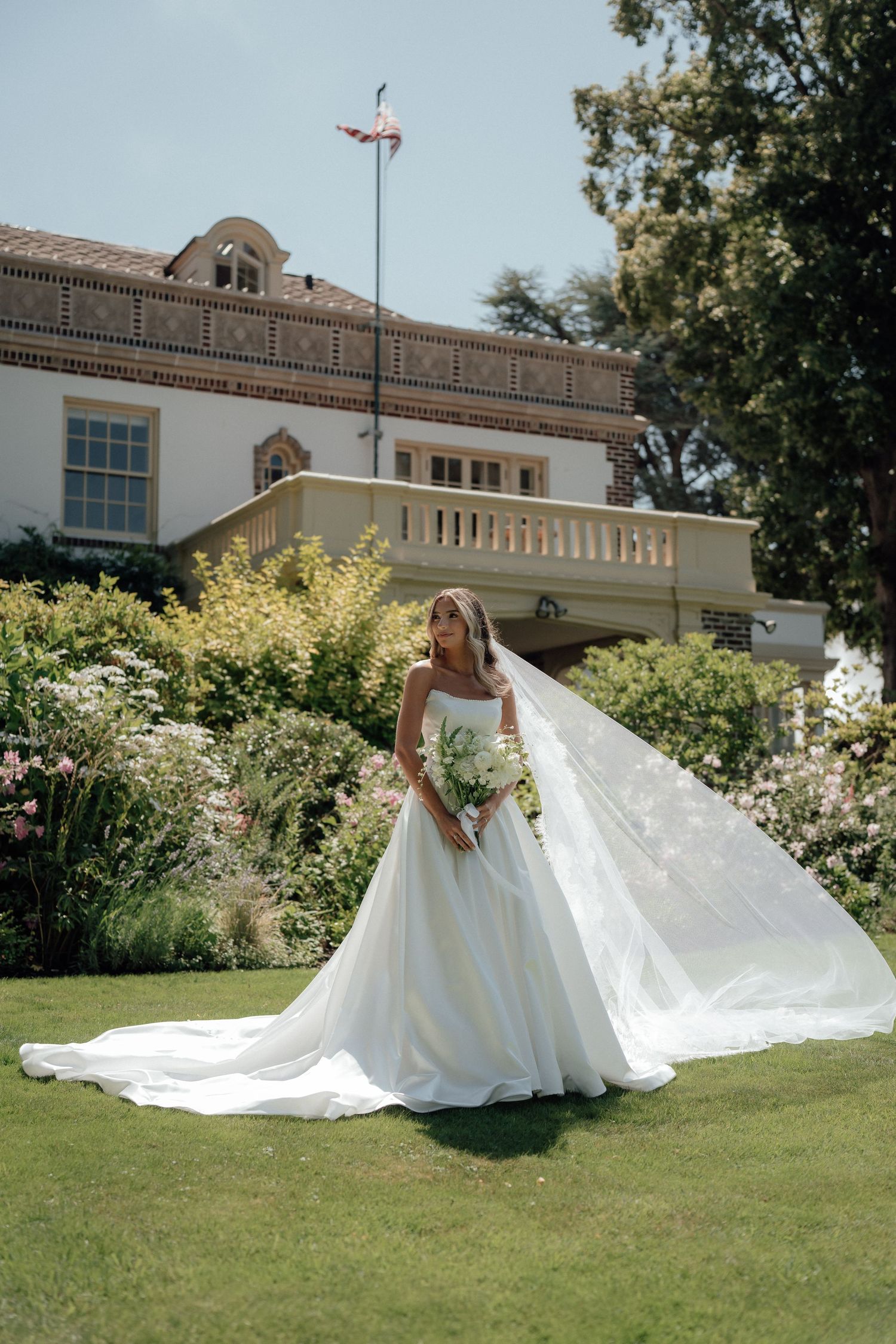 A stunning bridal portrait on manicured grounds with a flowing white gown and classic architecture backdrop.