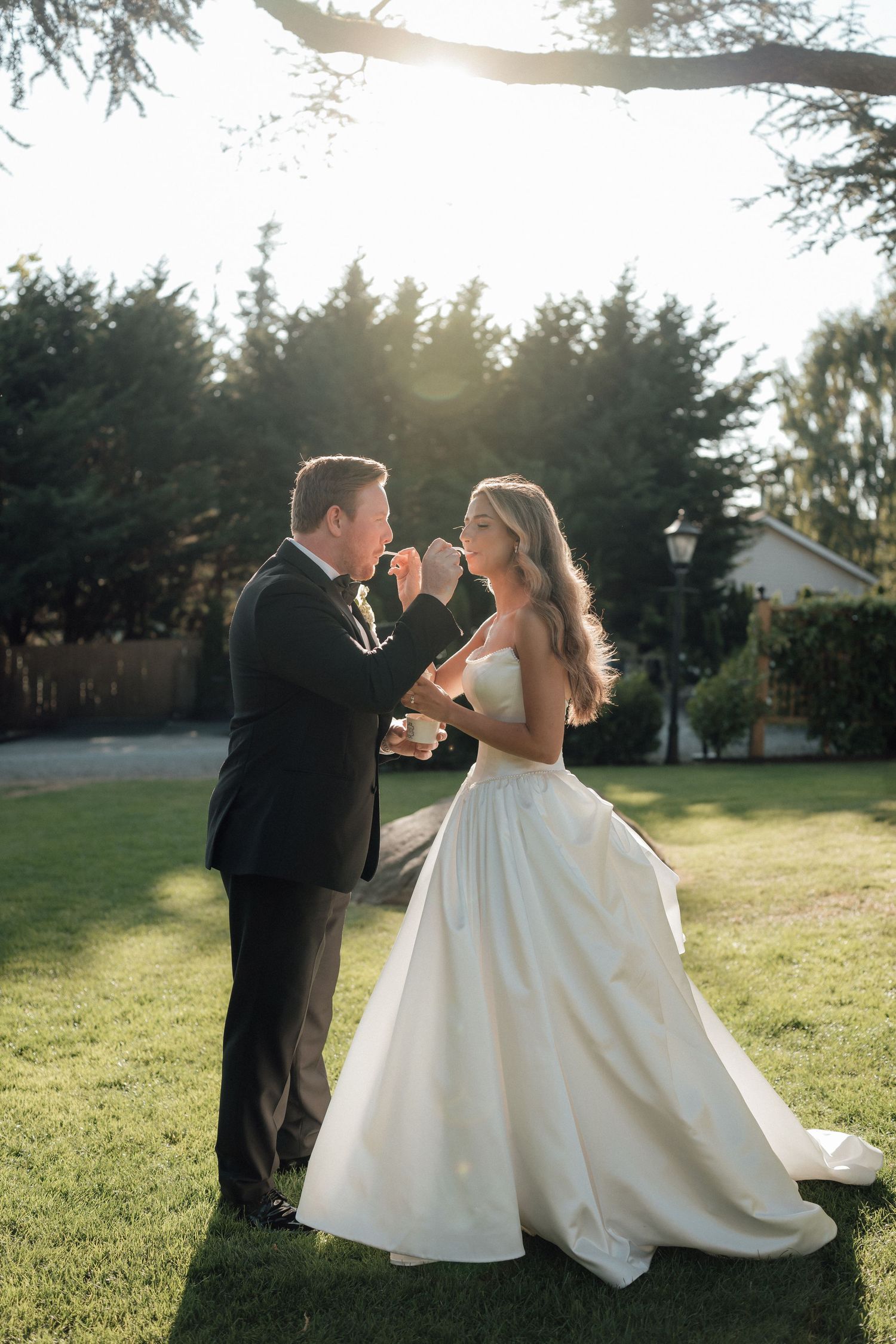 A romantic sunset wedding photo shows a couple dancing together on a lawn with evergreen trees in the background.