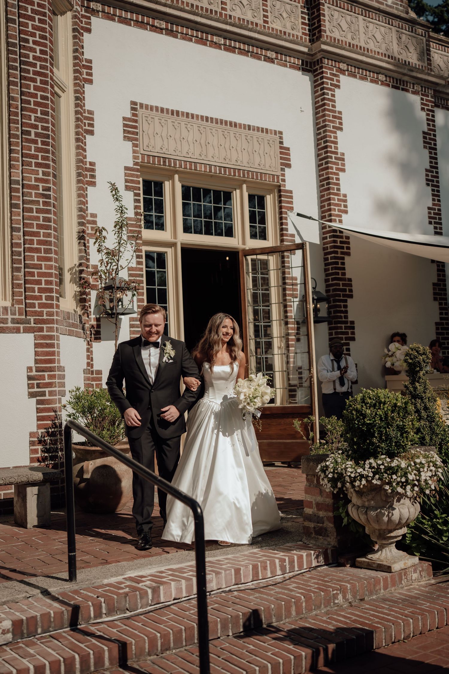 A couple descends brick steps outside an elegant brick building during their wedding ceremony.