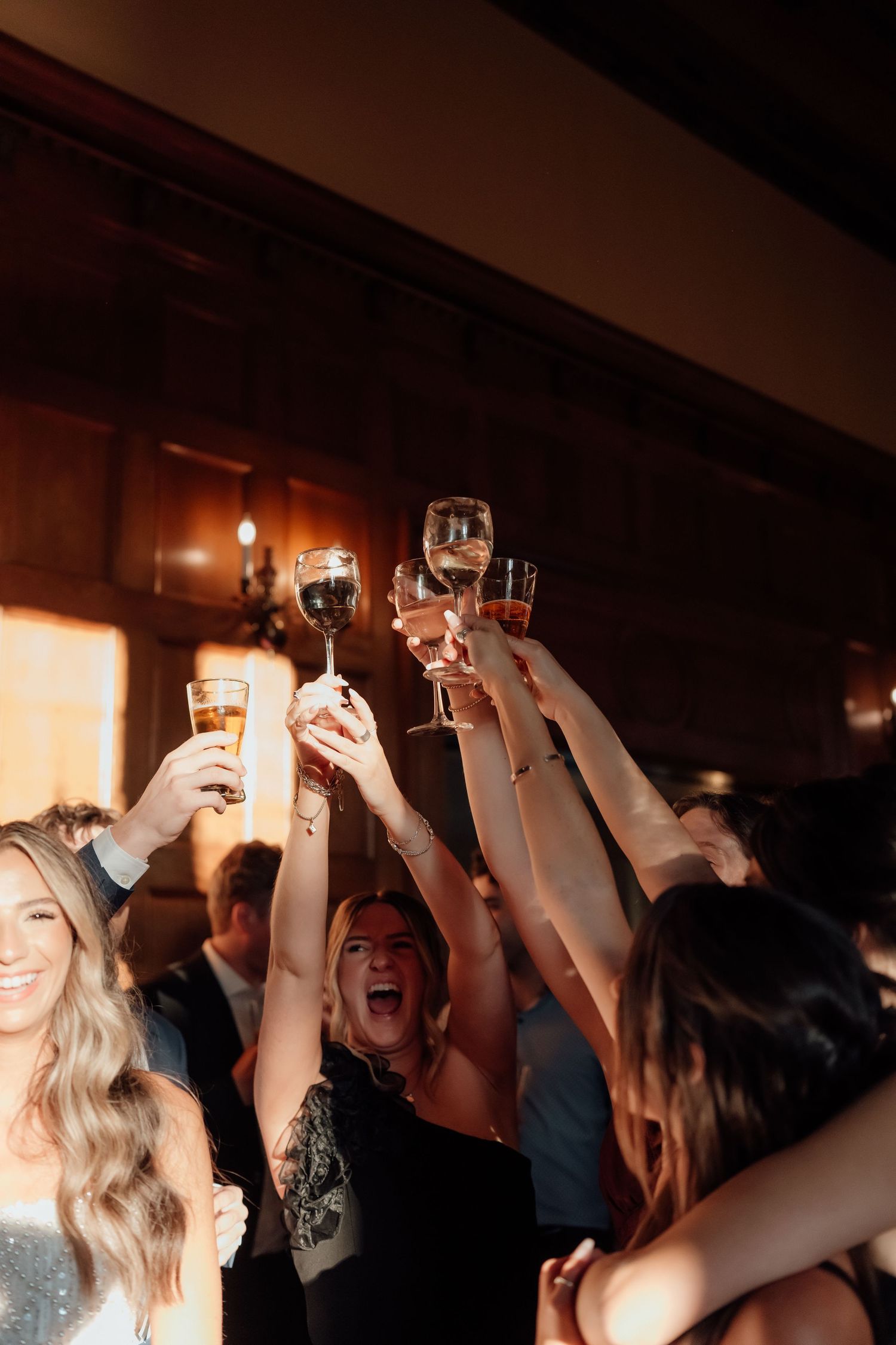A crowd holds up their drinks in celebration at a dimly lit party venue.