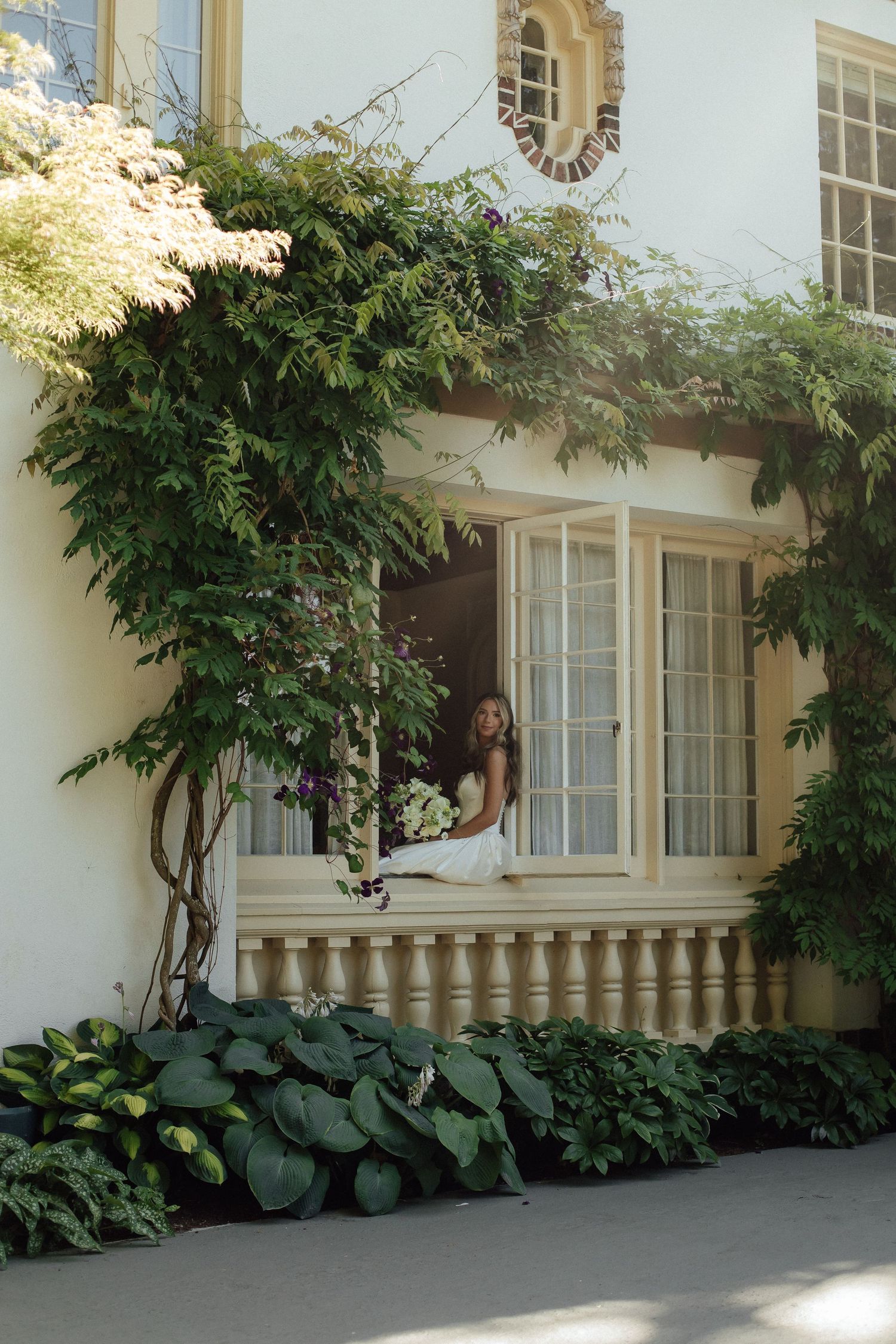 Classic white mansion window with climbing vines and ornate balcony creating a romantic setting.