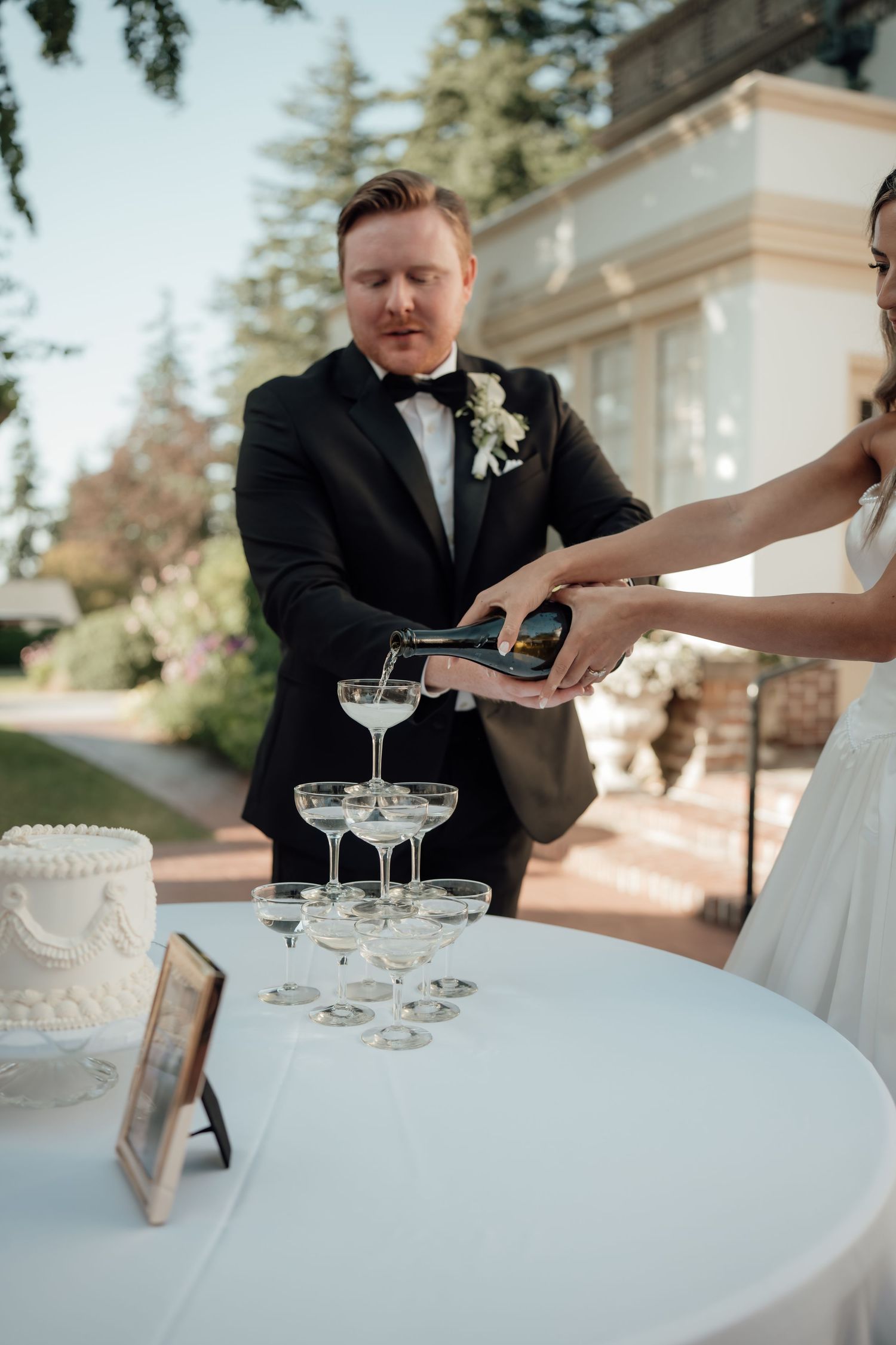 Wedding guests pour champagne into vintage coupe glasses arranged on a white tablecloth.