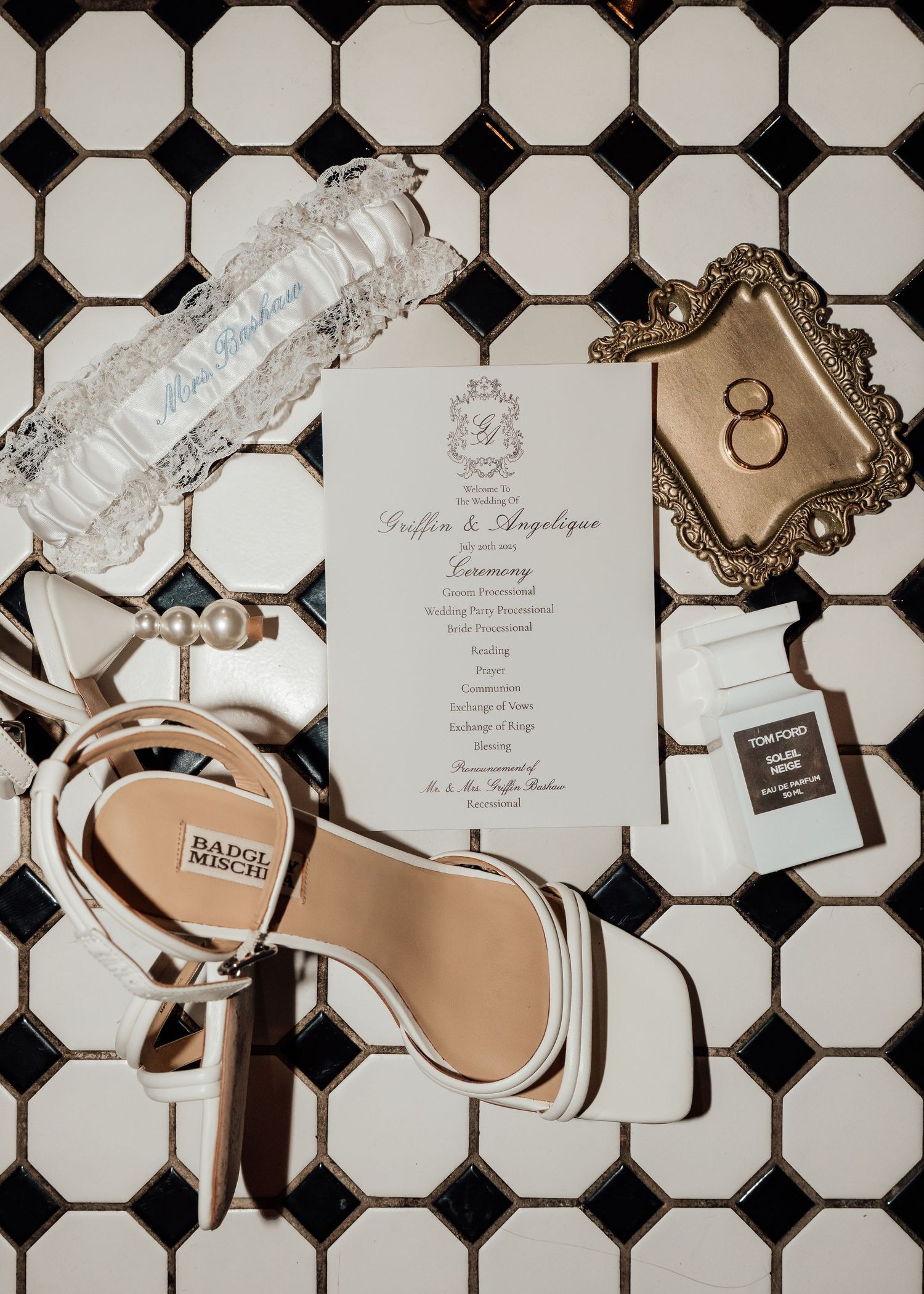 Wedding invitations and elegant bridal shoes arranged on a black and white tile floor.