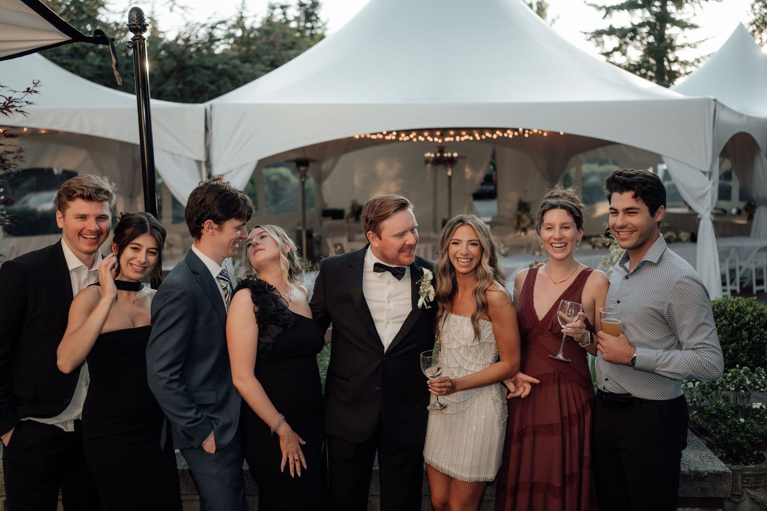 Wedding party celebrates under white tent canopies at outdoor evening reception.