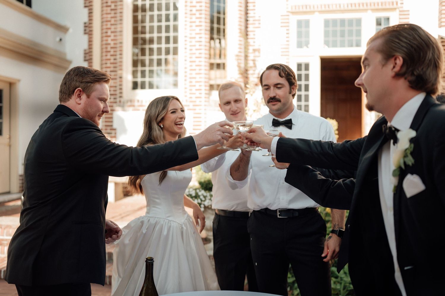 Wedding party toasting with champagne glasses outside elegant venue.
