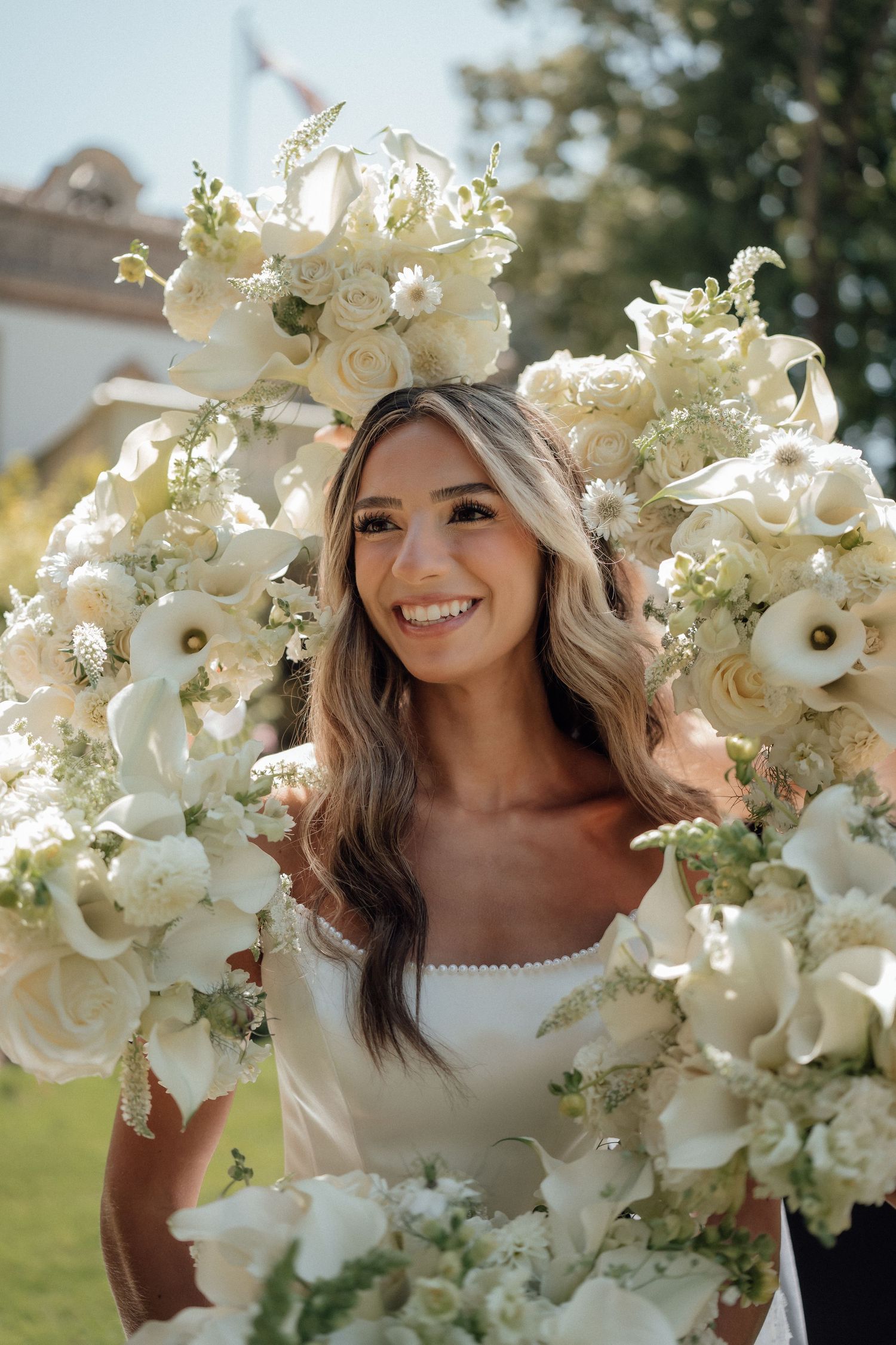 A stunning wedding bouquet of white roses and orchids frames a bridal portrait in an outdoor garden setting.