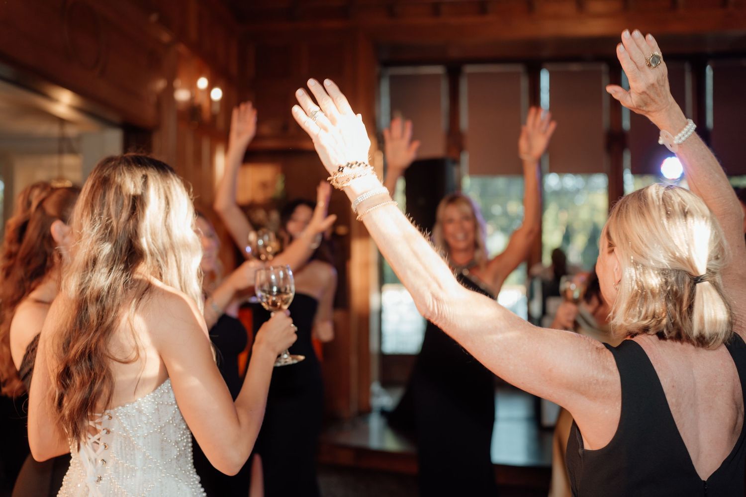 Wedding guests dancing and celebrating with raised hands in a dimly lit reception venue.