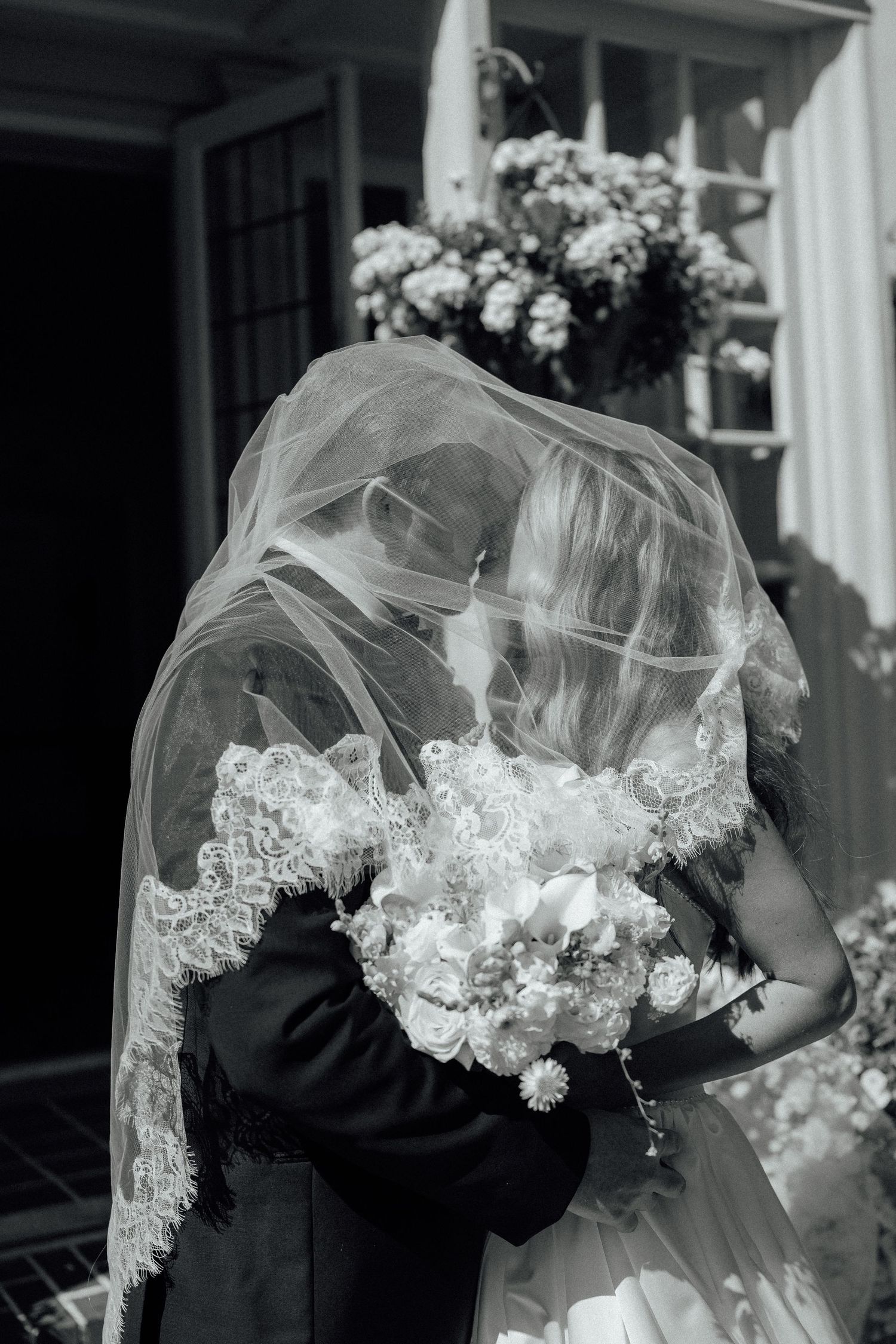 A romantic black and white wedding photograph showing a couple sharing an intimate moment under a delicate lace veil.