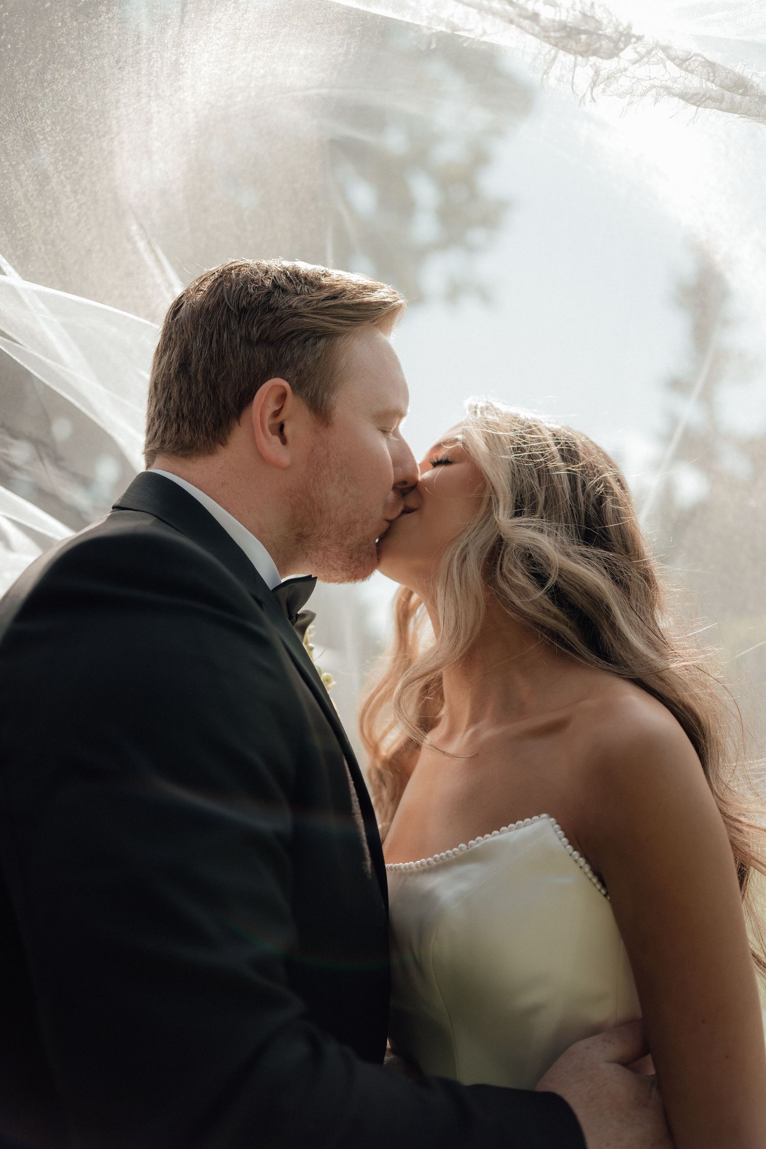 A tender moment between newlyweds captured under a flowing white veil.