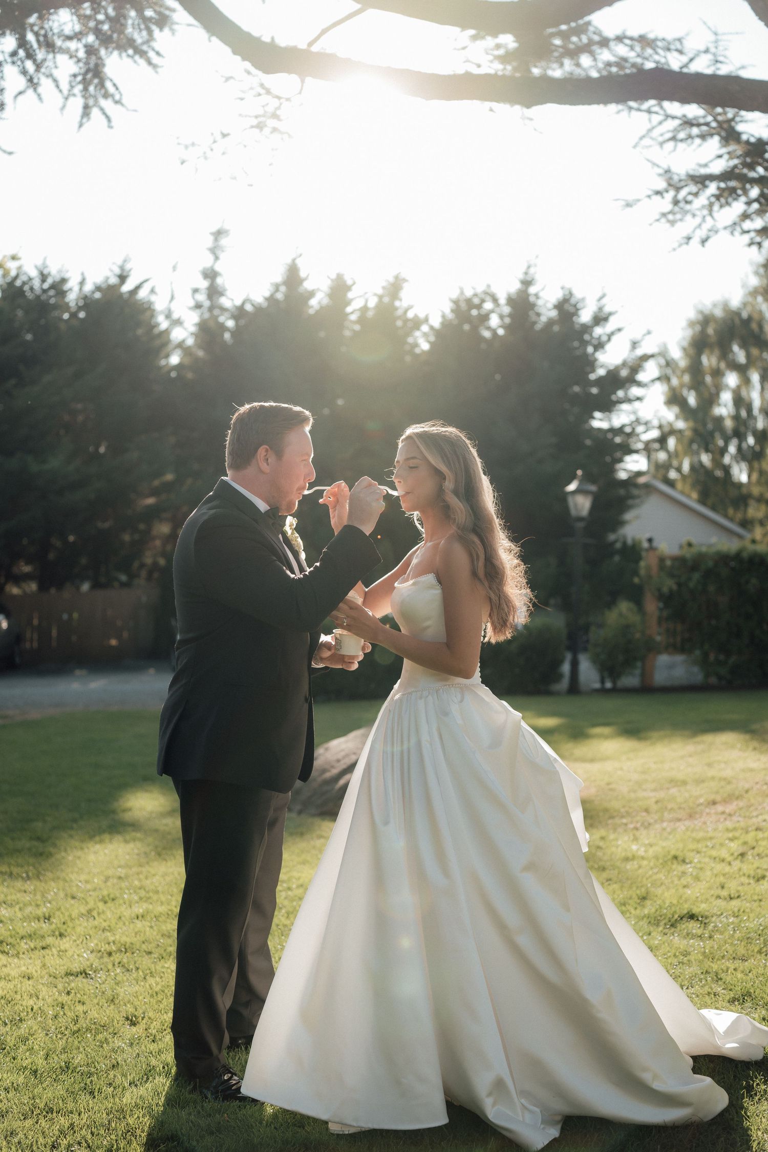 A romantic sunset dance between newlyweds on a green lawn with trees in the background.