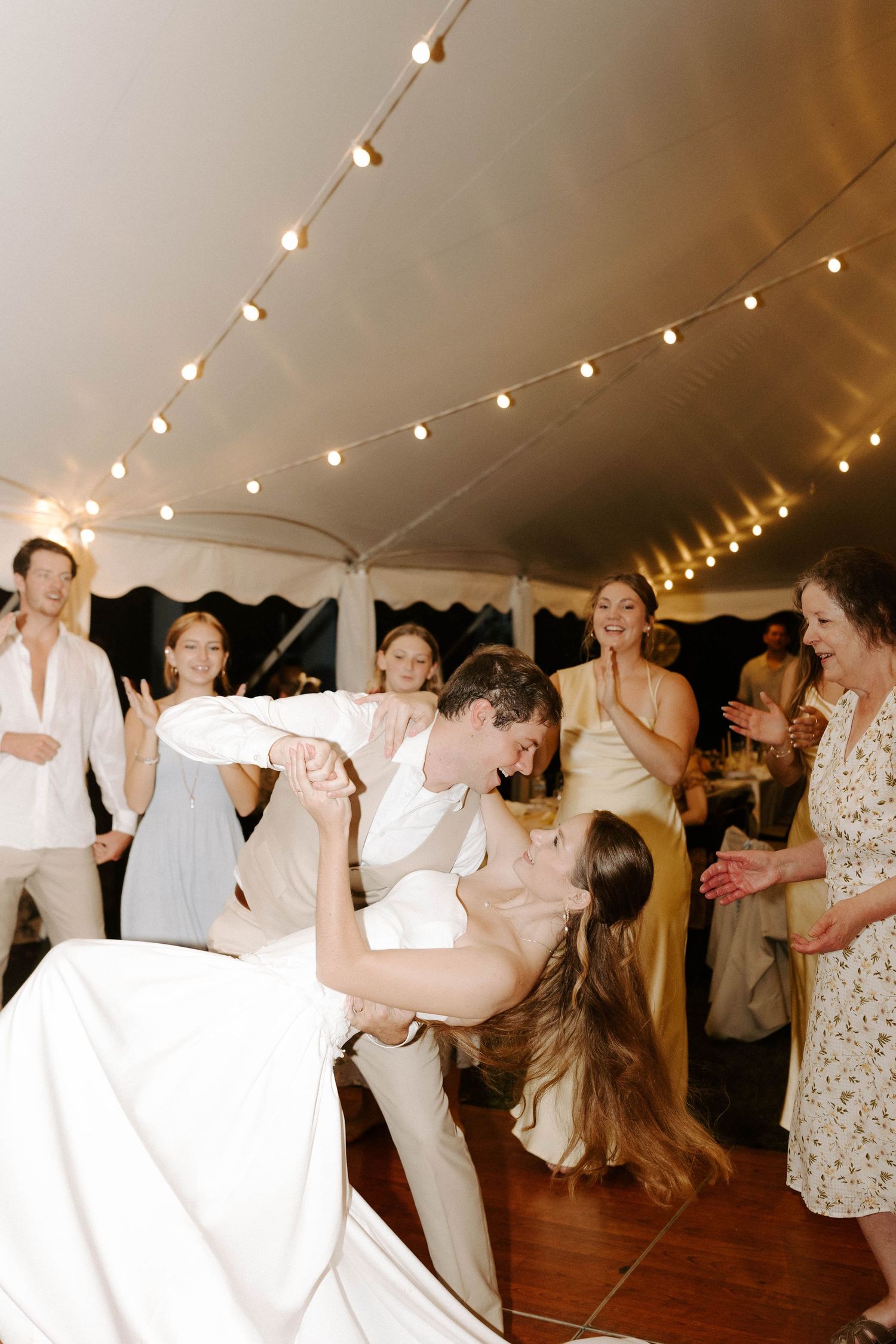 A bride and groom share a romantic dip kiss on the dance floor at their wedding reception under string lights.