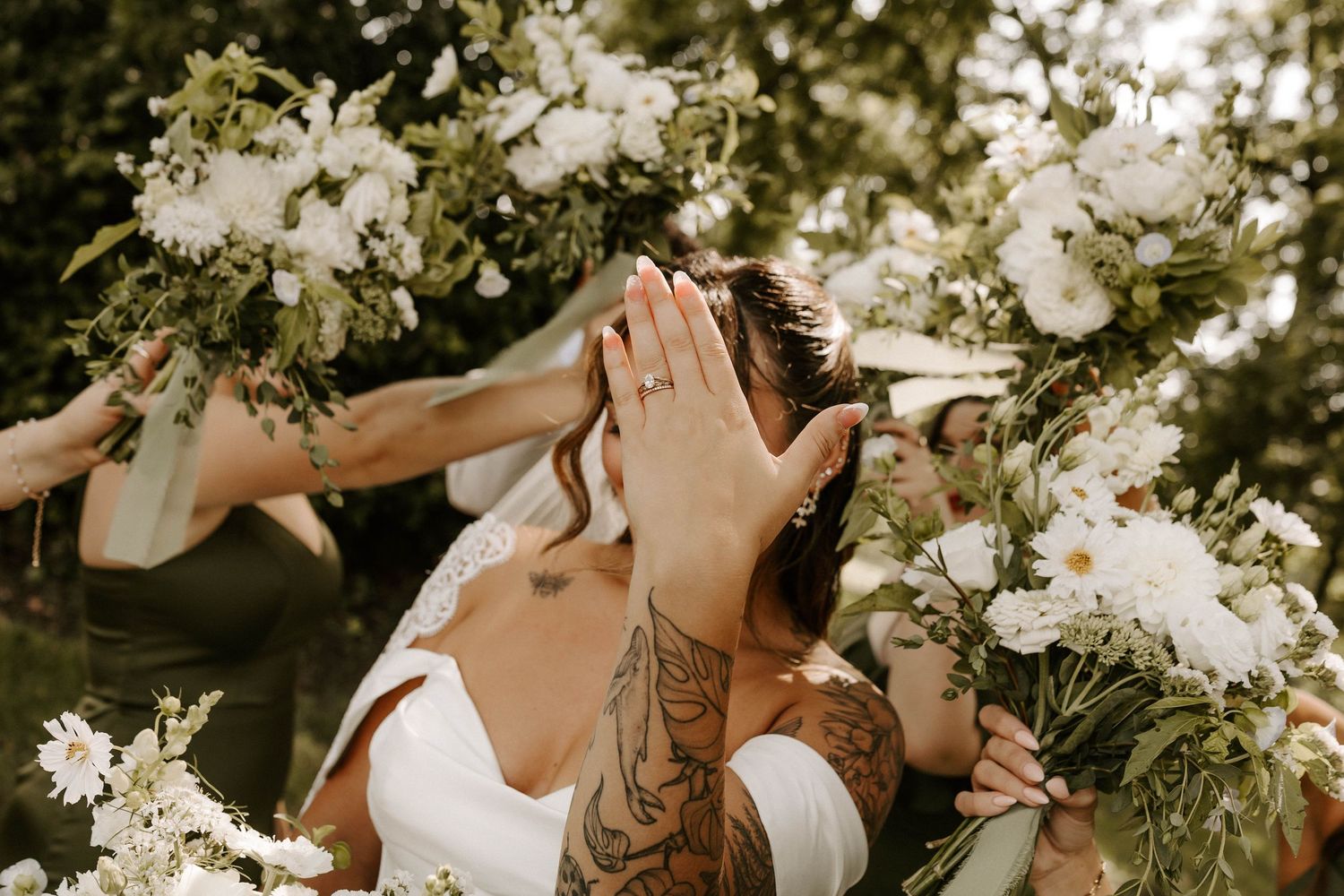 Bride and groom sharing a kiss surrounded by white floral bouquets held by bridesmaids outdoors.