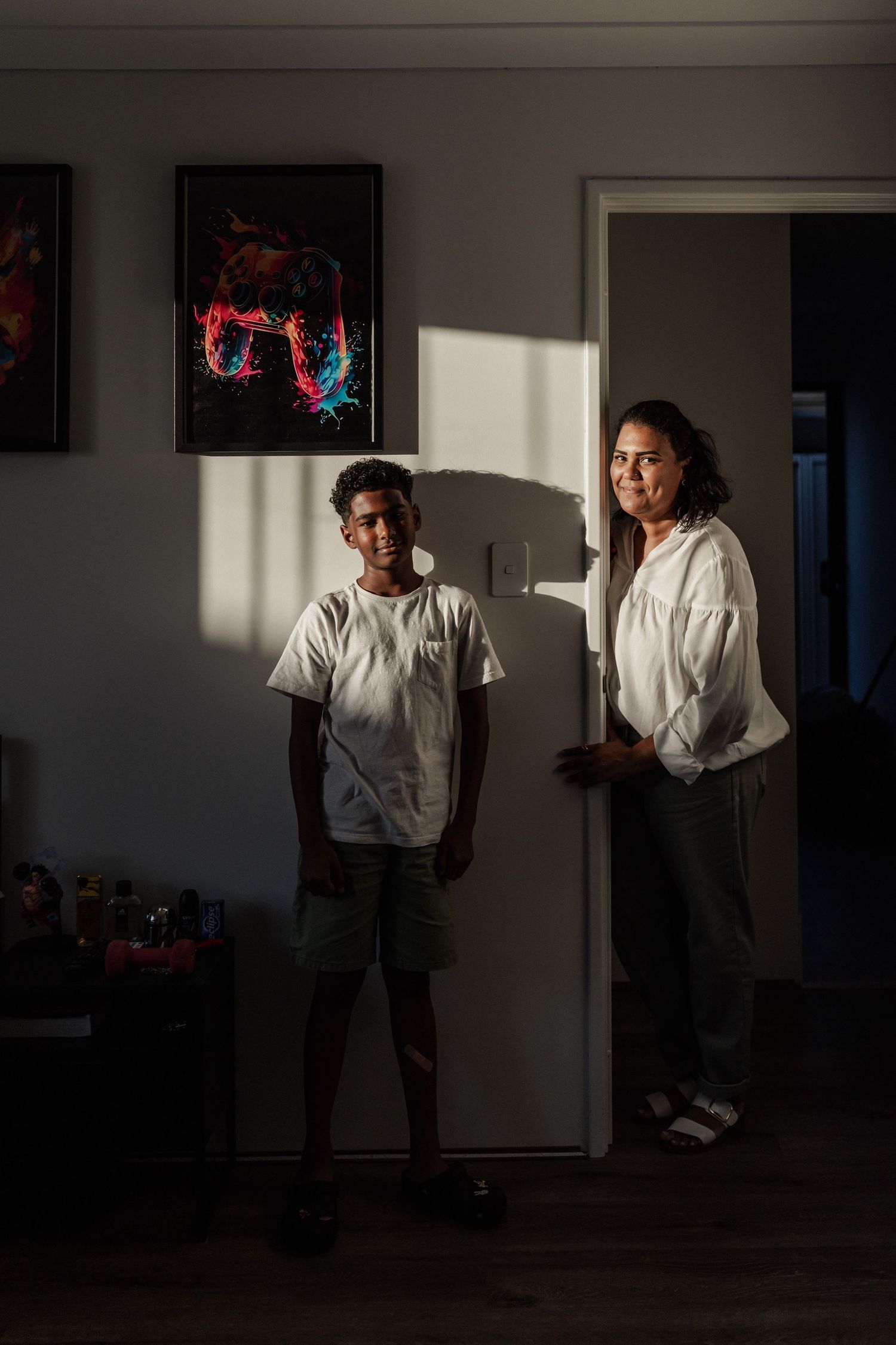 A South African mum and teenage son, looking at the family photographer. Both are standing in a patch of light, leaning against the wall.