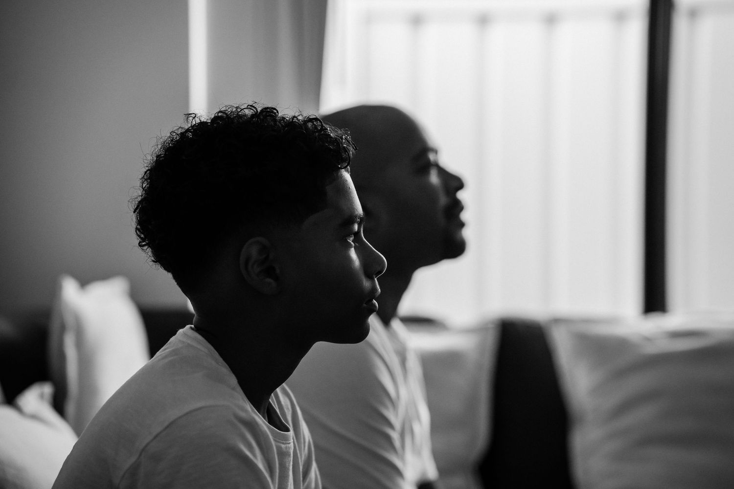 A teenage boy and his dad look towards a screen while playing a computer game. Only their side profiles are in the photo.