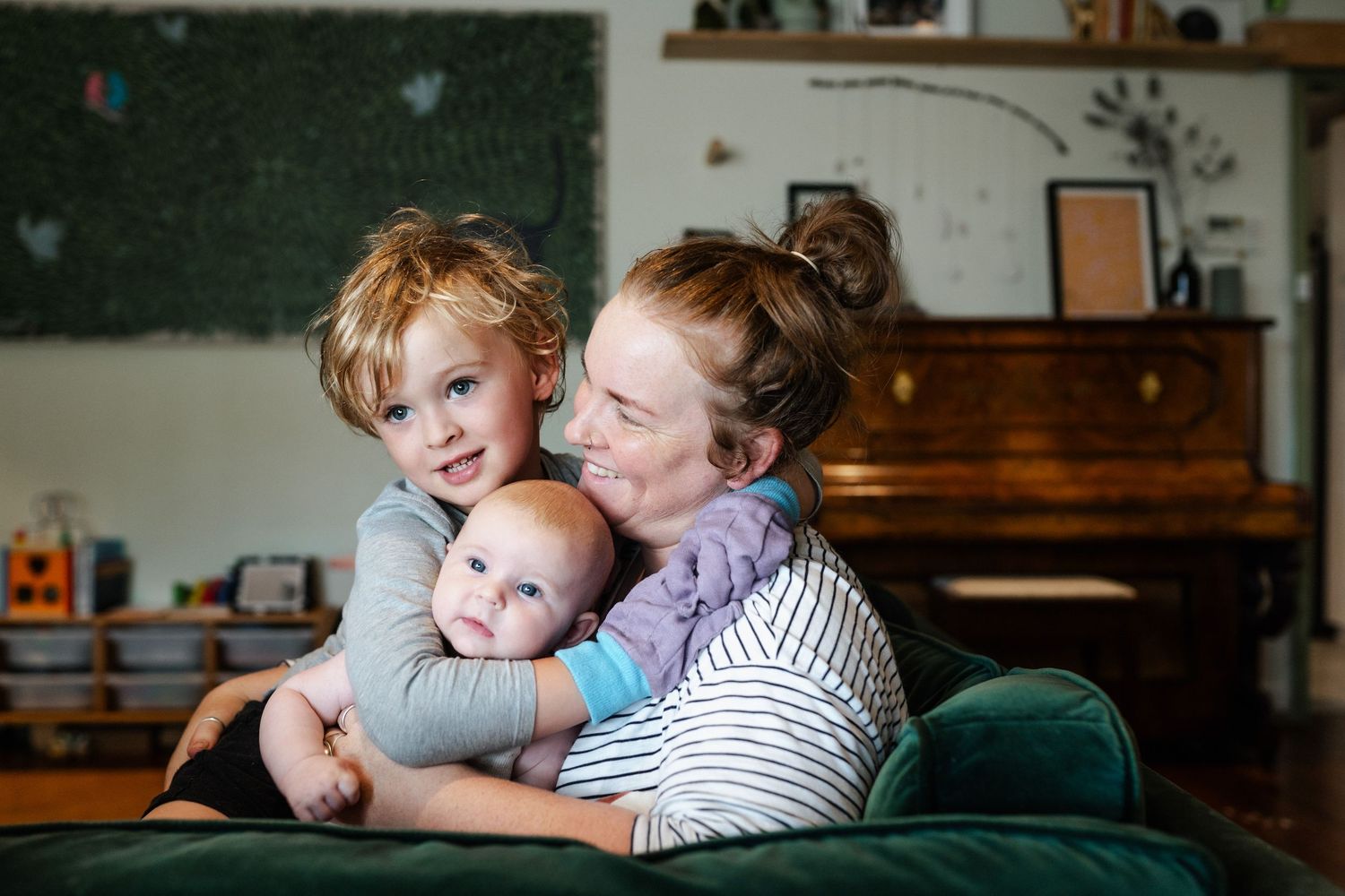 A mum sits on her couch with her son and baby daughter, cuddling.