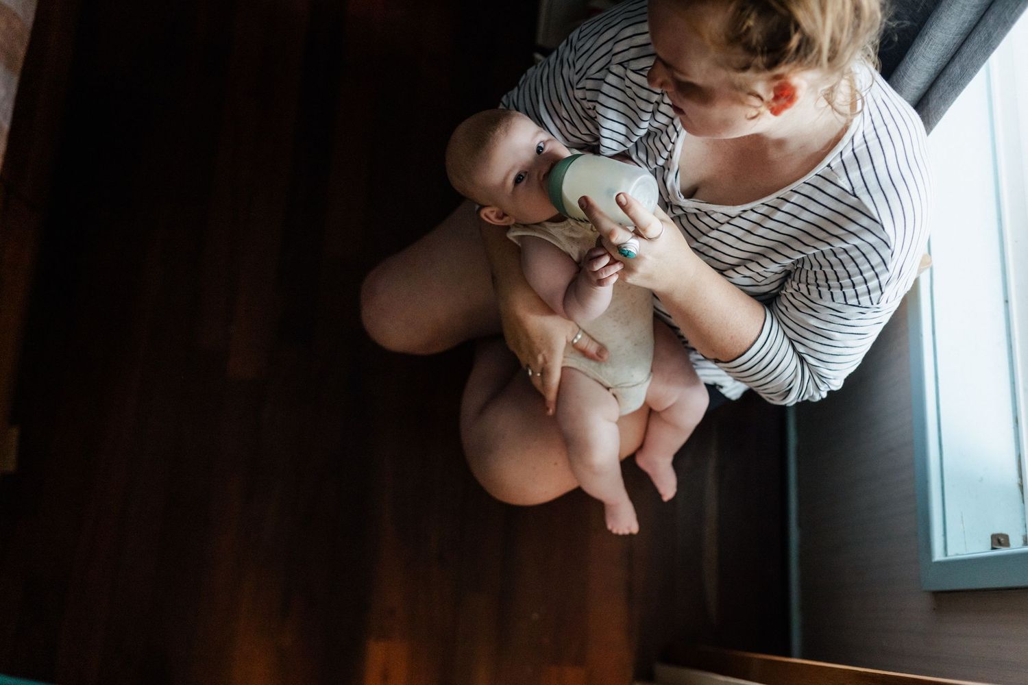A Birds Eye view of a mum feeding her baby a bottle of milk. The baby is looking directly at the family photographer.
