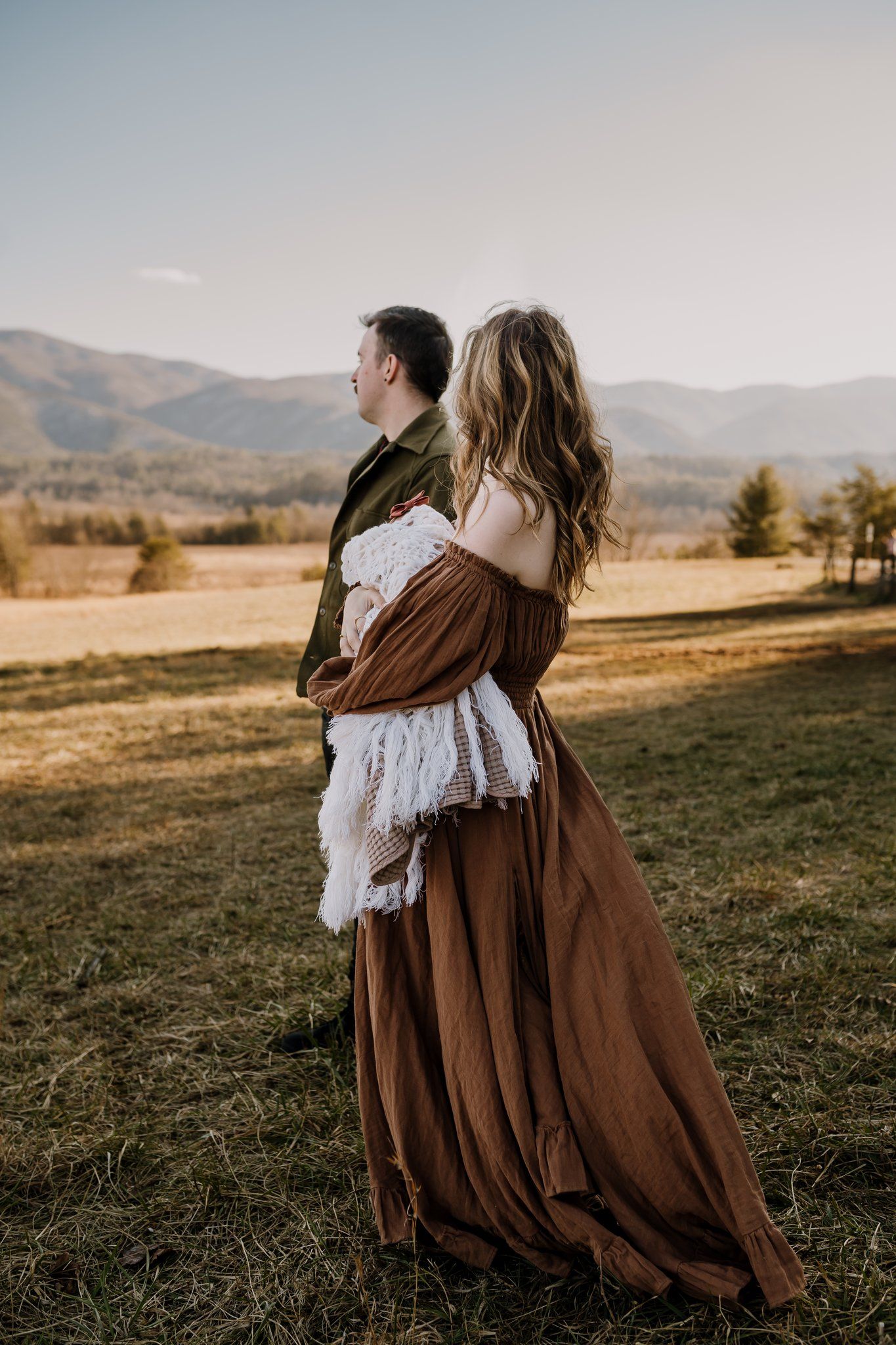 Mom and dad walk through field together holding baby girl