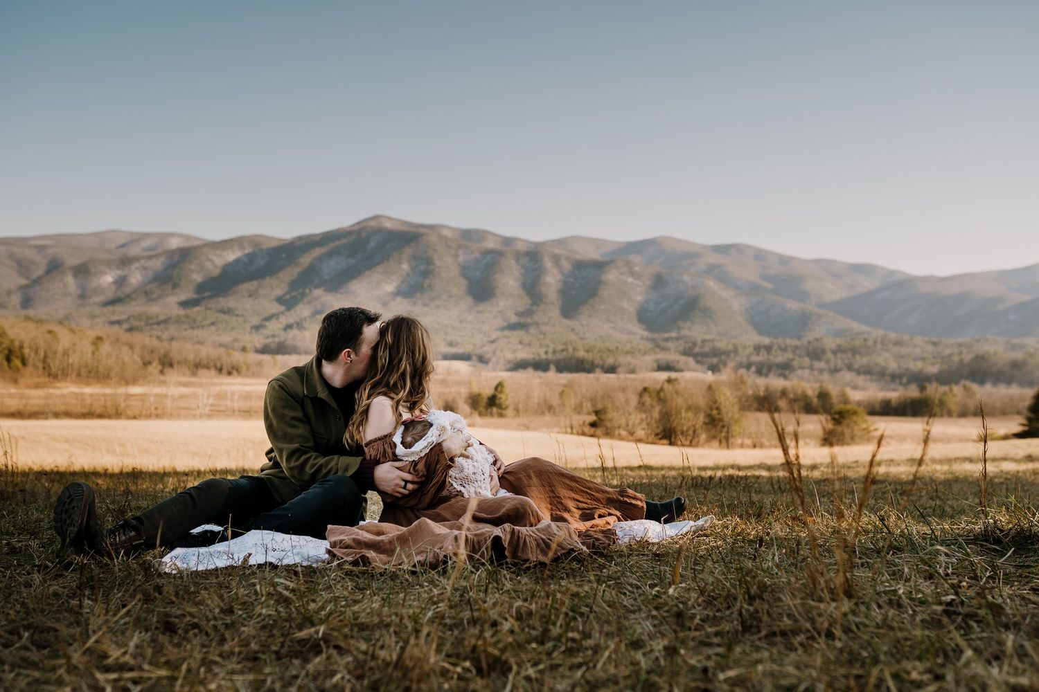 Family sits at Cades Cove admiring the Great Smoky Mountains during family pictures