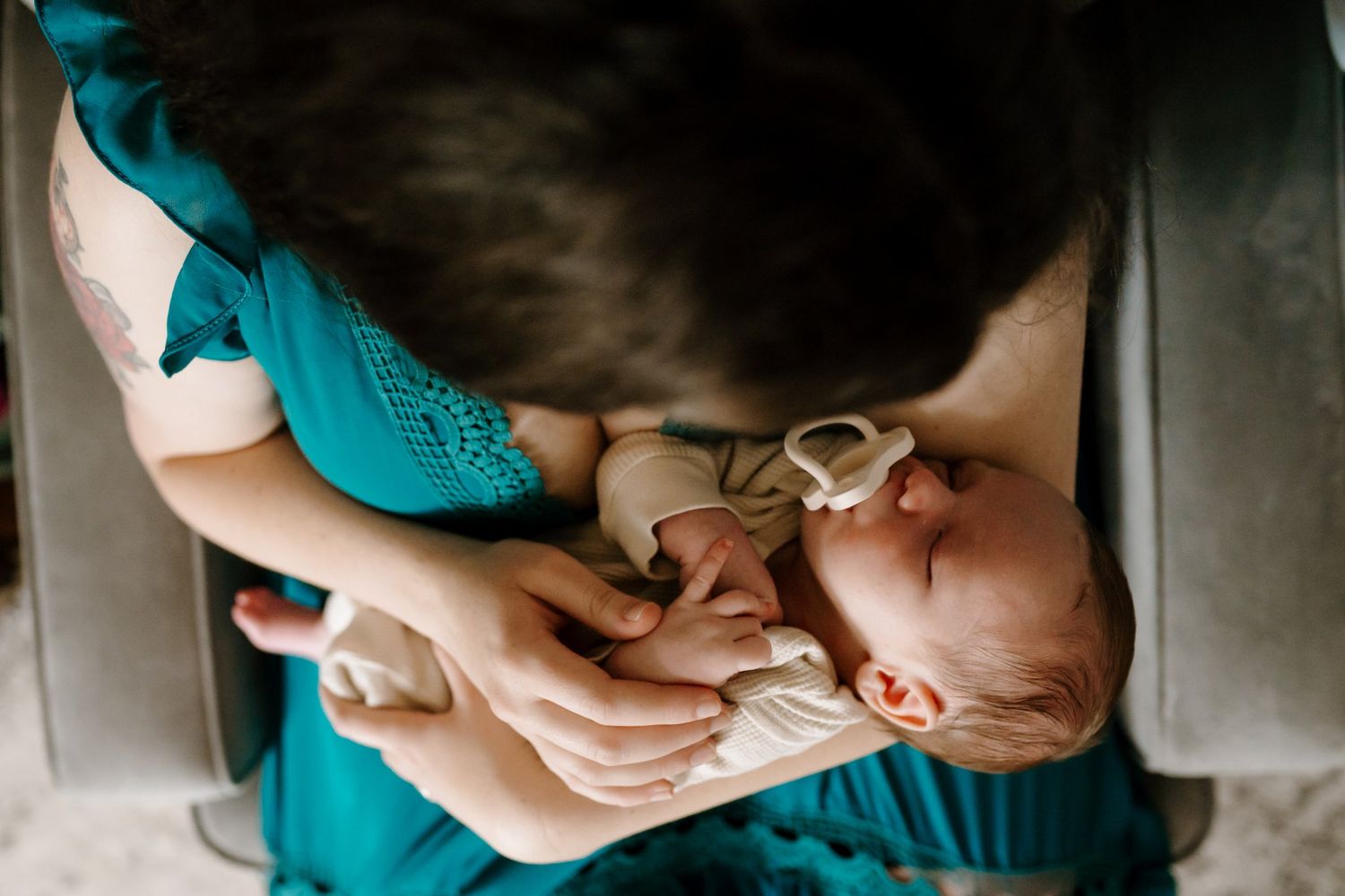Newborn baby in mom's arms as she sits in nursery chair