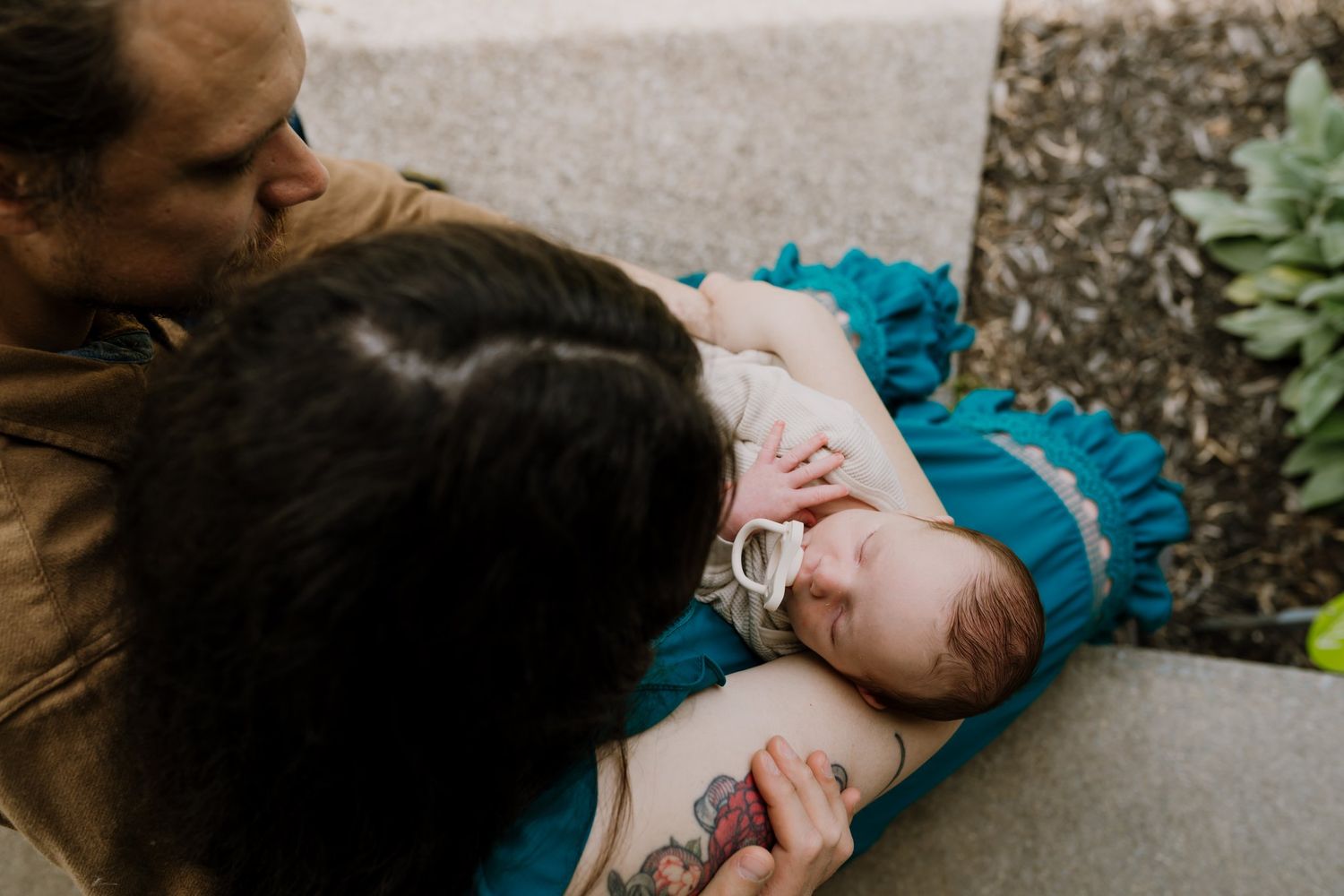 Parents cradle newborn baby as they sit on their front porch