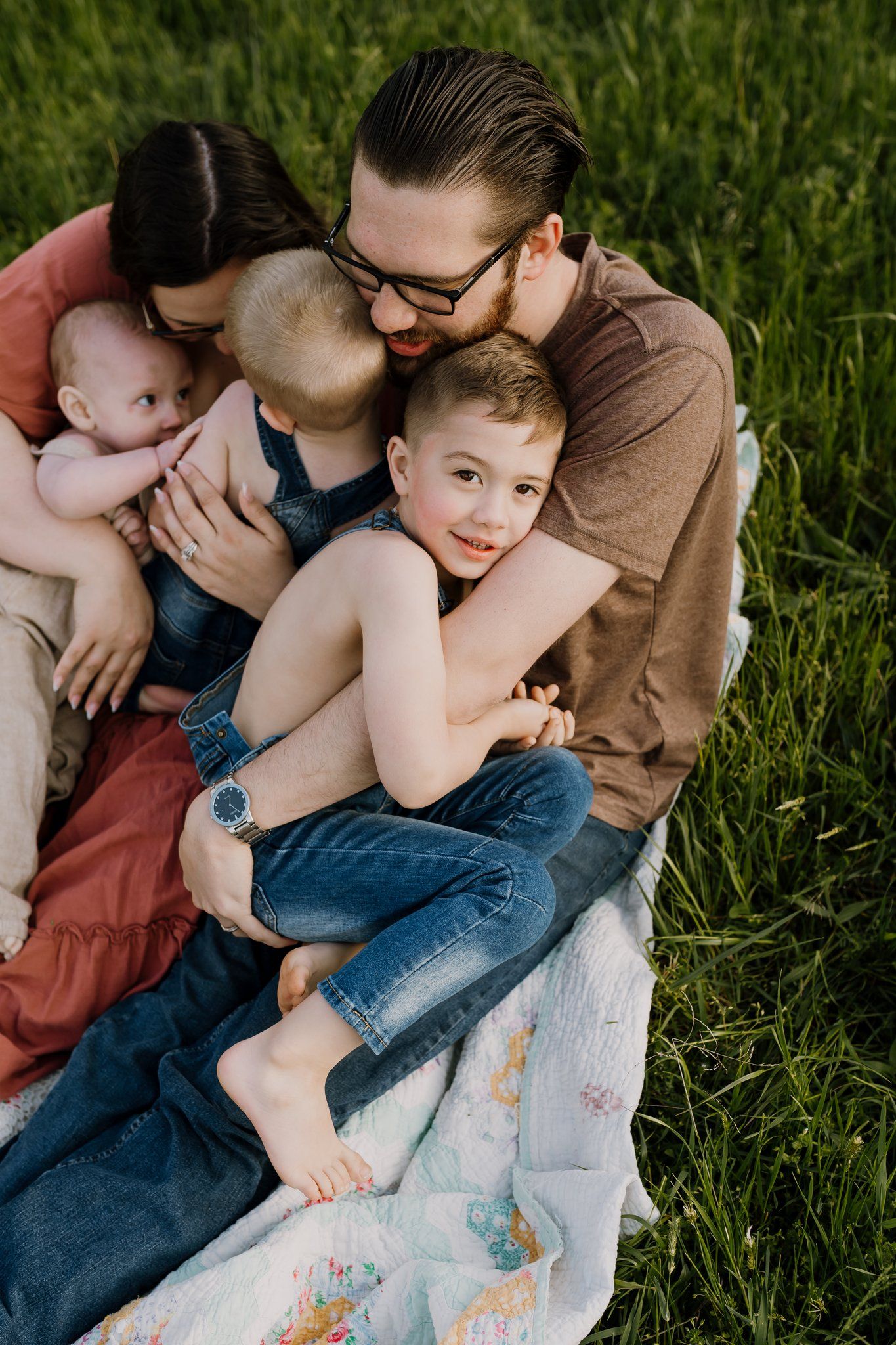 Family snuggles in a field on a blanket at golden hour