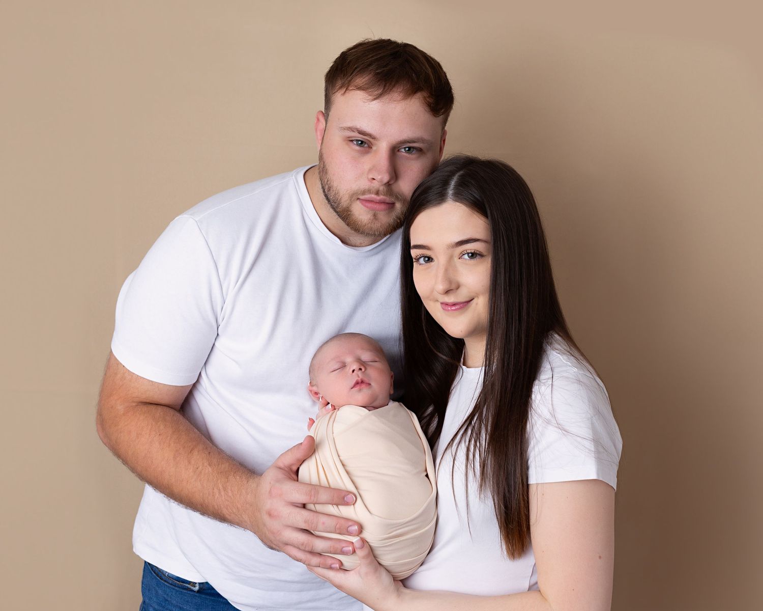 Family photoshoot, new mum and dad holding wrapped baby, all wearing white
