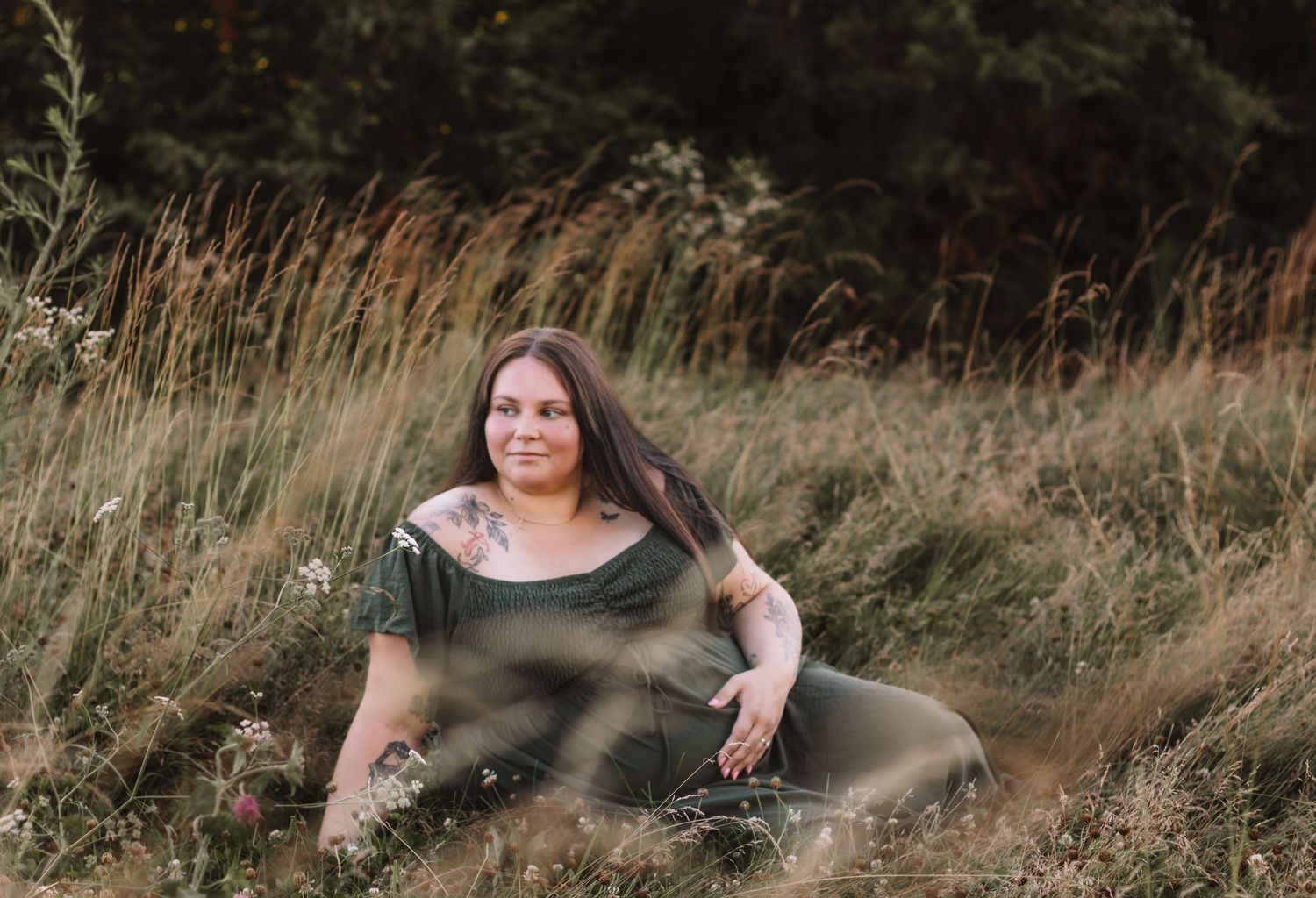 expecting mother sitting in an open field holding her baby bump