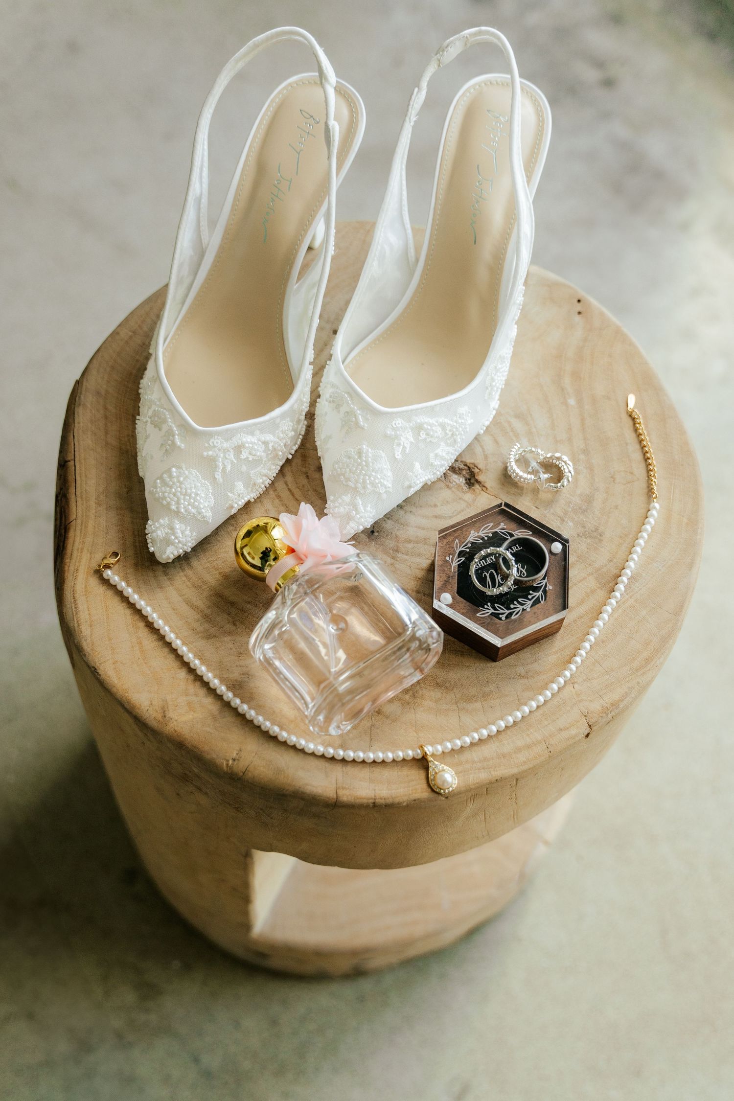 White bridal shoes with pearl accessories and perfume bottle displayed on wooden round platform in multiple angles.
