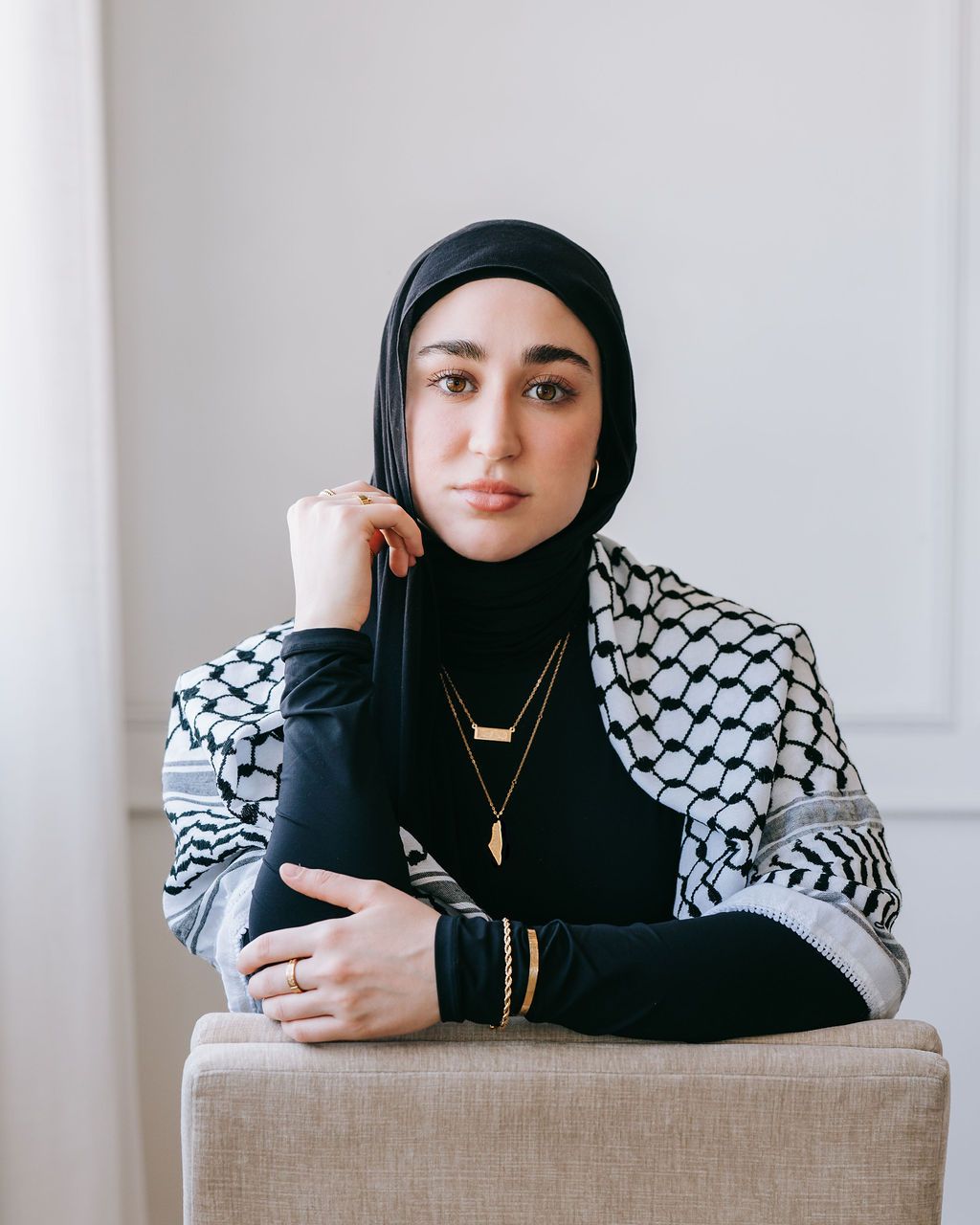 Person in black and patterned keffiyeh style top poses against neutral background.
