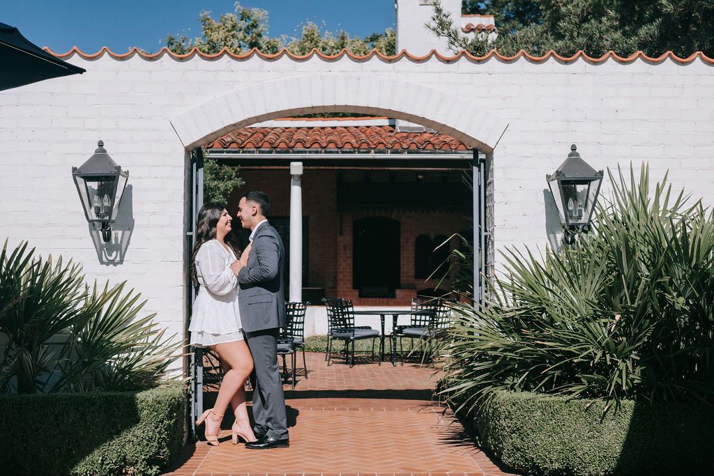 Couple shares intimate moment by Spanish-style building with lanterns.