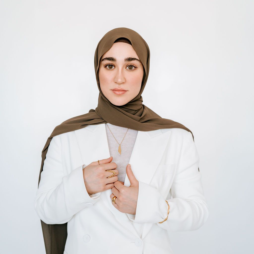 Portrait against white background showcasing modern modest fashion in white and olive tones.
