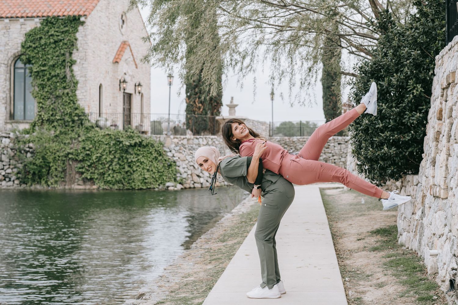Person performing a balance pose along a waterfront path near an ivy-covered building.