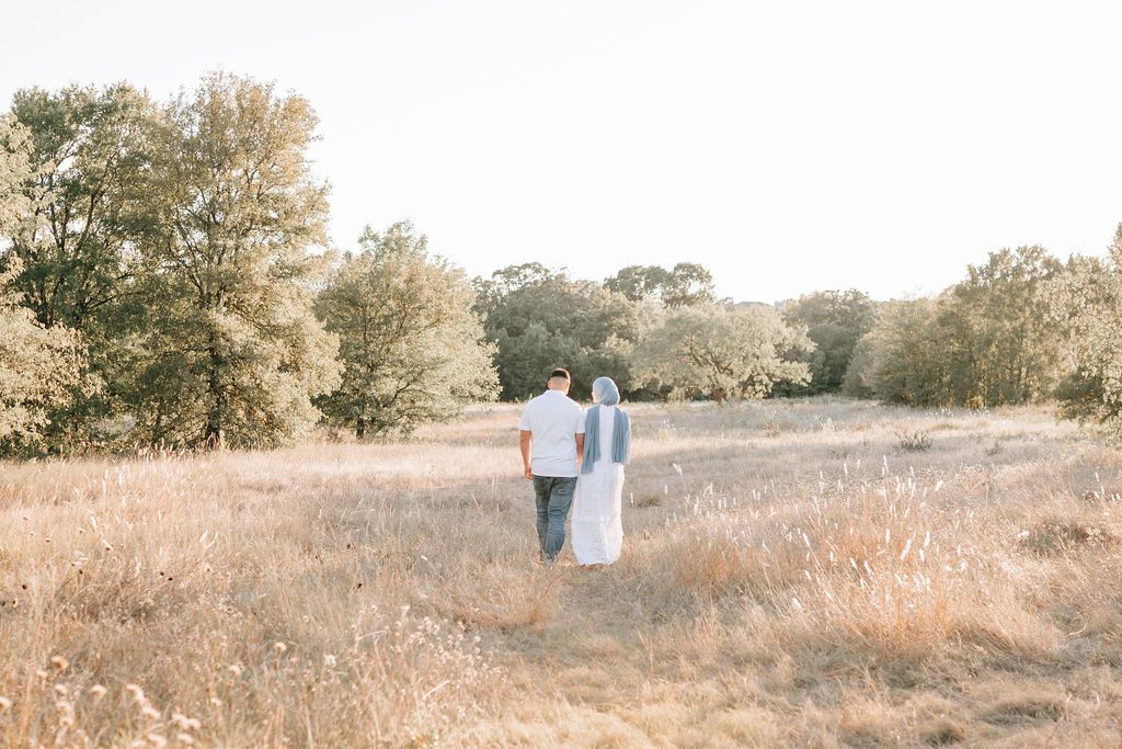 Couple walking together in distance across golden field at sunset.