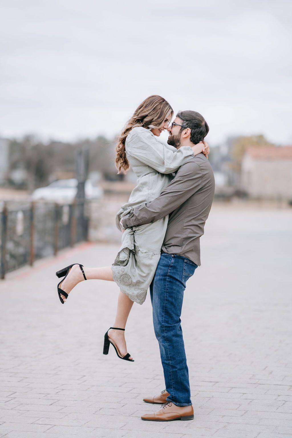 Playful couple embracing on urban walkway with woman in heels lifted by partner.