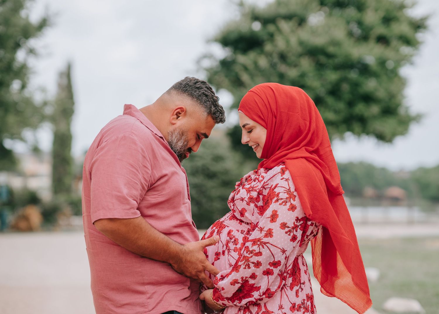 Couple in casual attire sharing tender moment outdoors during maternity photoshoot.
