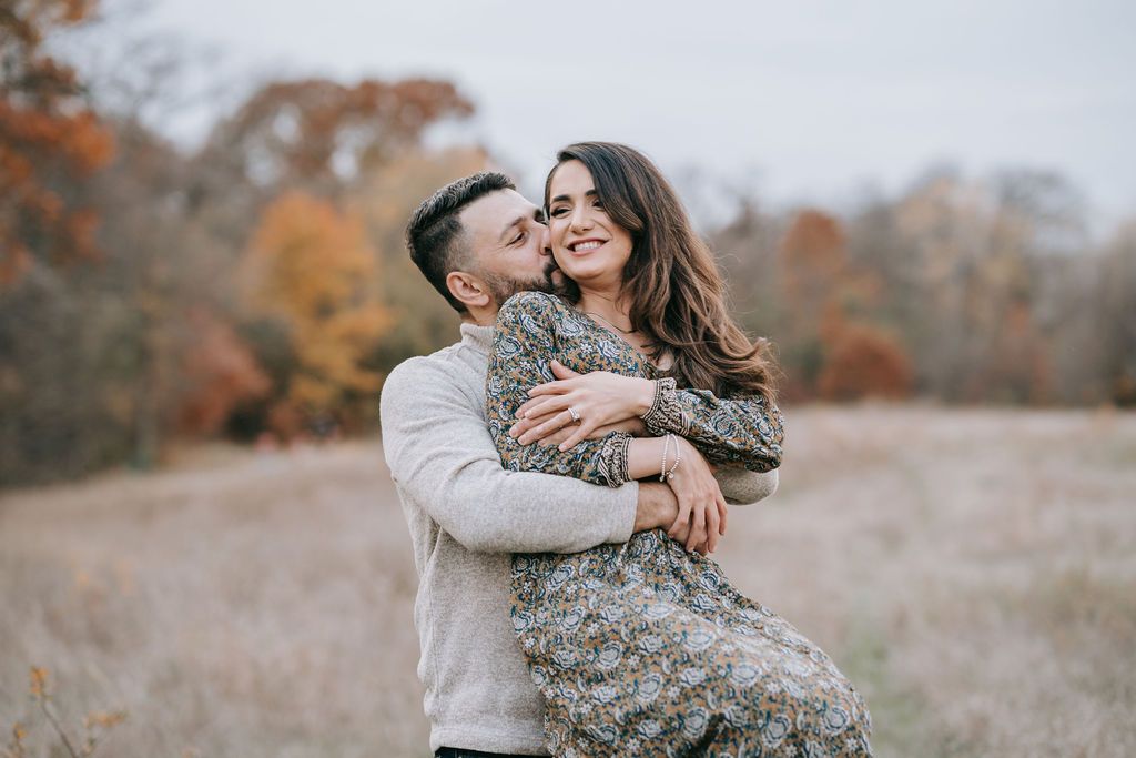 Joyful autumn outdoor portrait of couple embracing in casual wear with fall colors in background.
