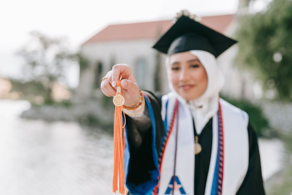 Graduation cap and tassel held up against blurred background.