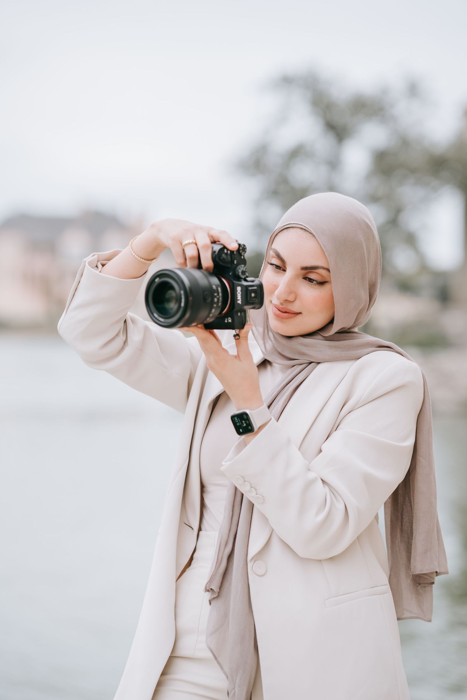 Photographer in beige hijab and suit jacket composing a shot with professional camera.
