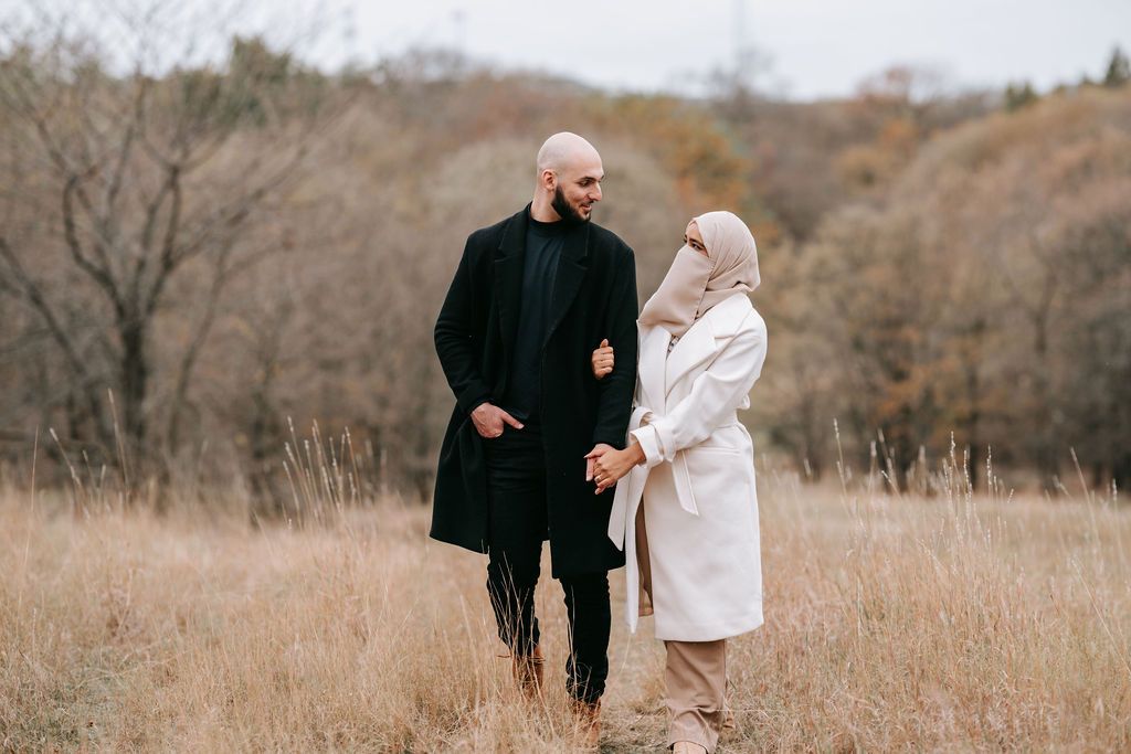 Couple in matching black and white coats stroll through autumn field.