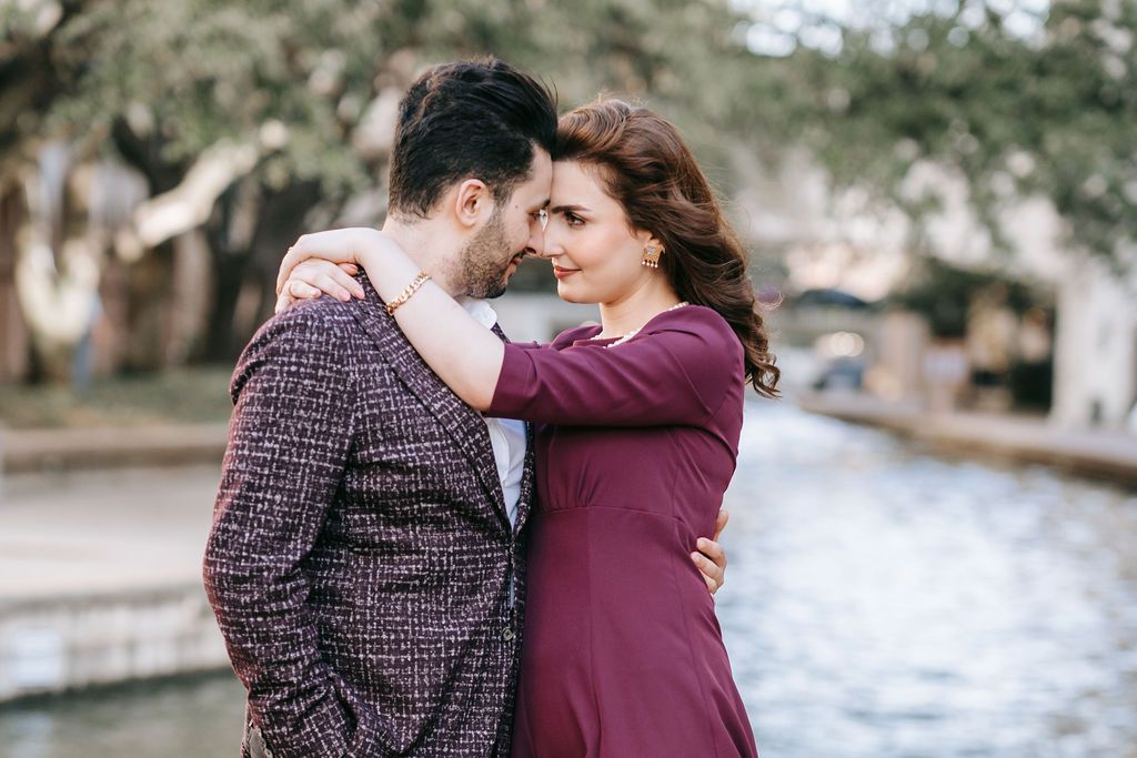 Couple in burgundy outfits sharing intimate moment by waterfront.