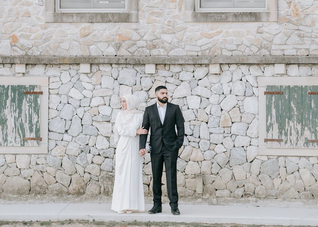 Formal portrait of couple in wedding attire against textured stone wall.