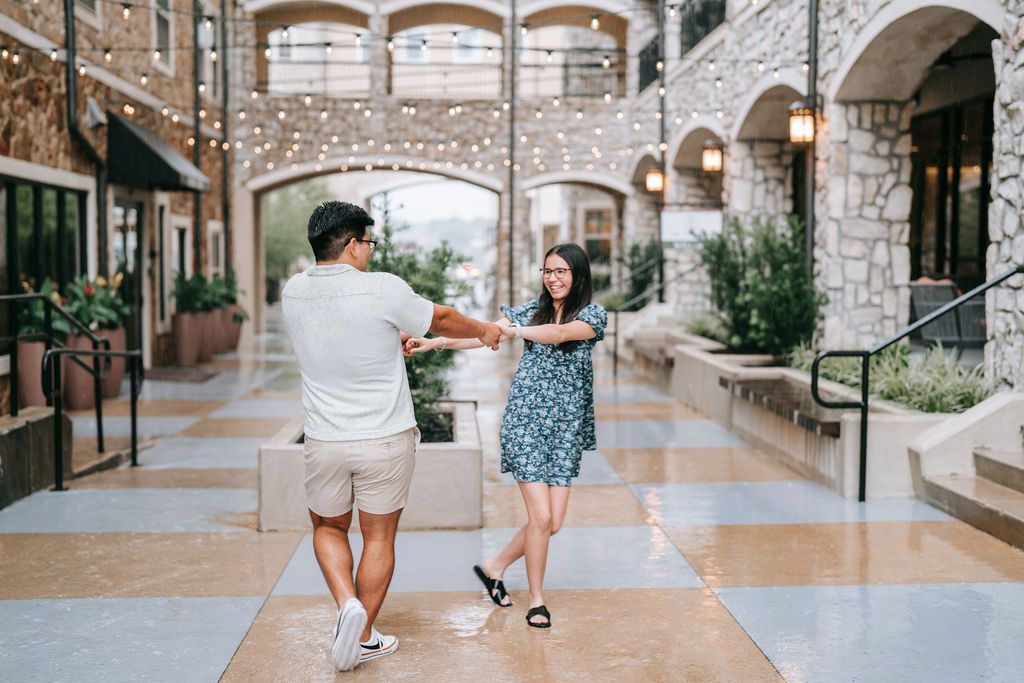 A couple dancing and twirling in an elegant stone archway corridor with string lights.