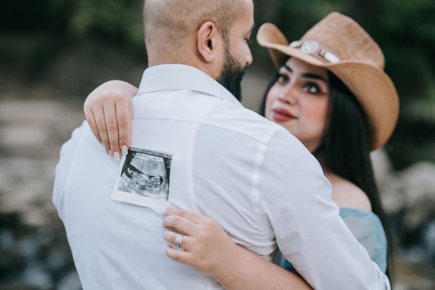 A couple shares an intimate moment while holding an ultrasound photo against a white shirt.